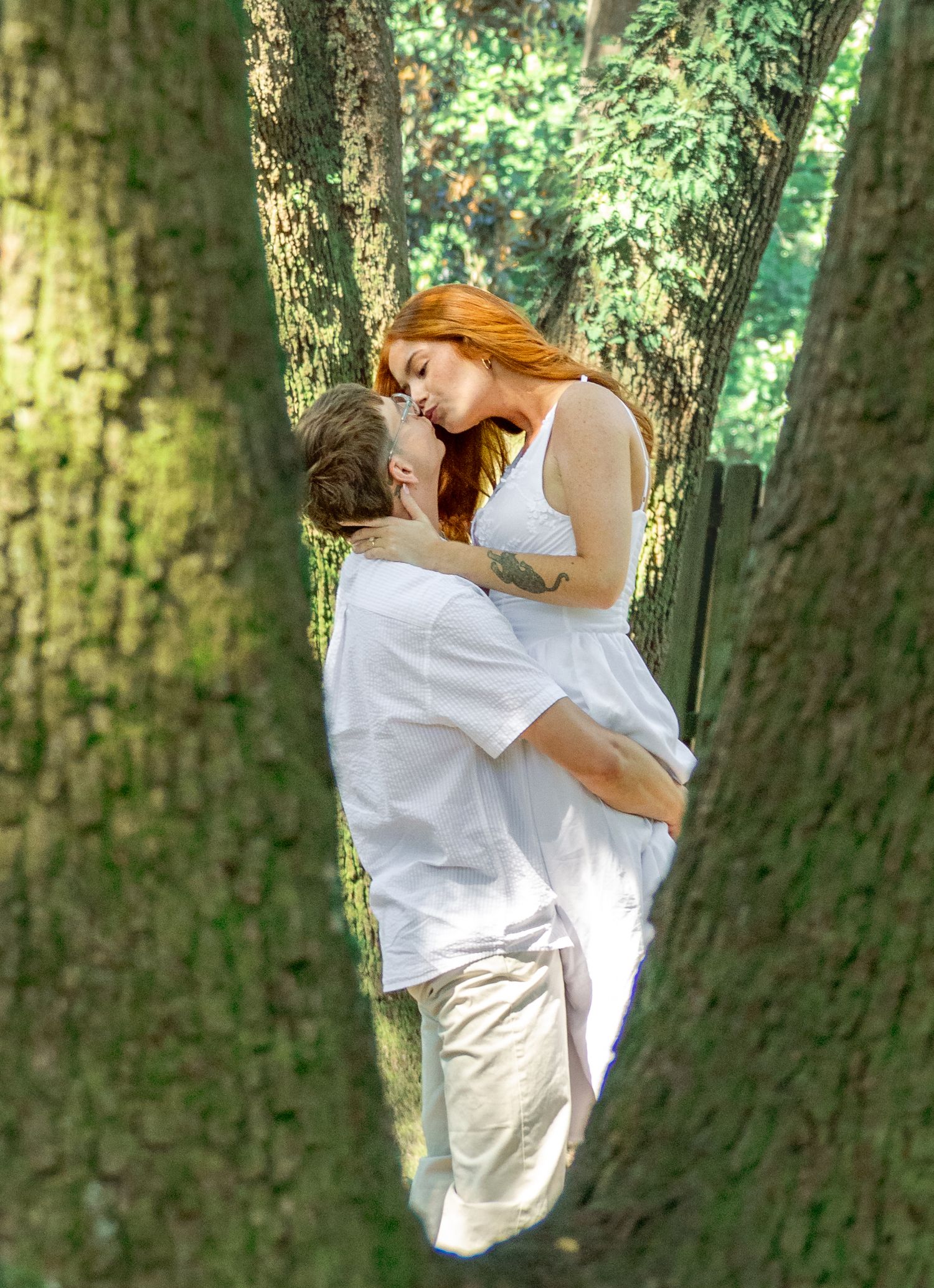Engaged couple sharing a kiss between large trees during an Aiken, South Carolina engagement session.
