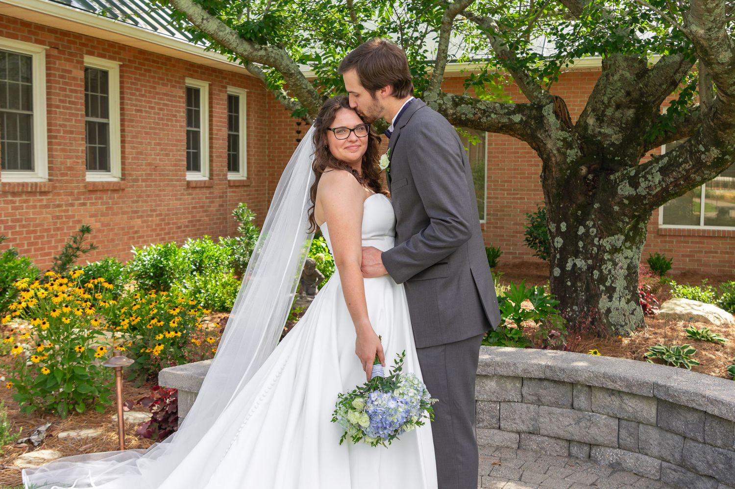 Bride and groom sharing a sweet moment outdoors on their South Carolina wedding day, with the bride holding a blue hydrangea bouquet.