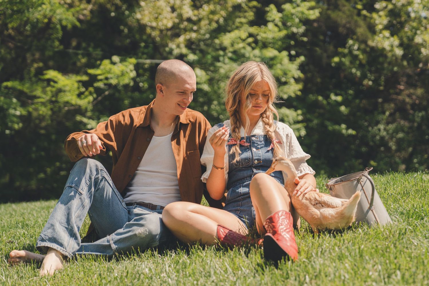 Young couple sitting on green grass in a sunny park, man pointing while woman listens attentively.