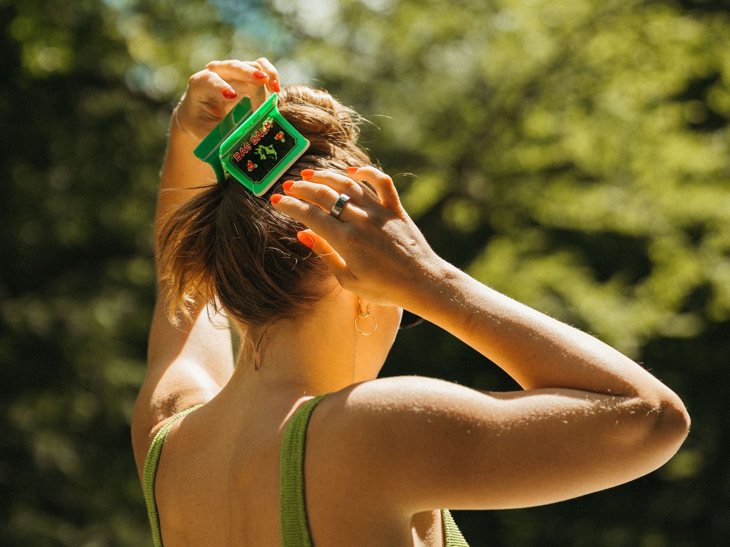 Close-up of woman styling hair with a green Bag Balm clip in sunny forest.