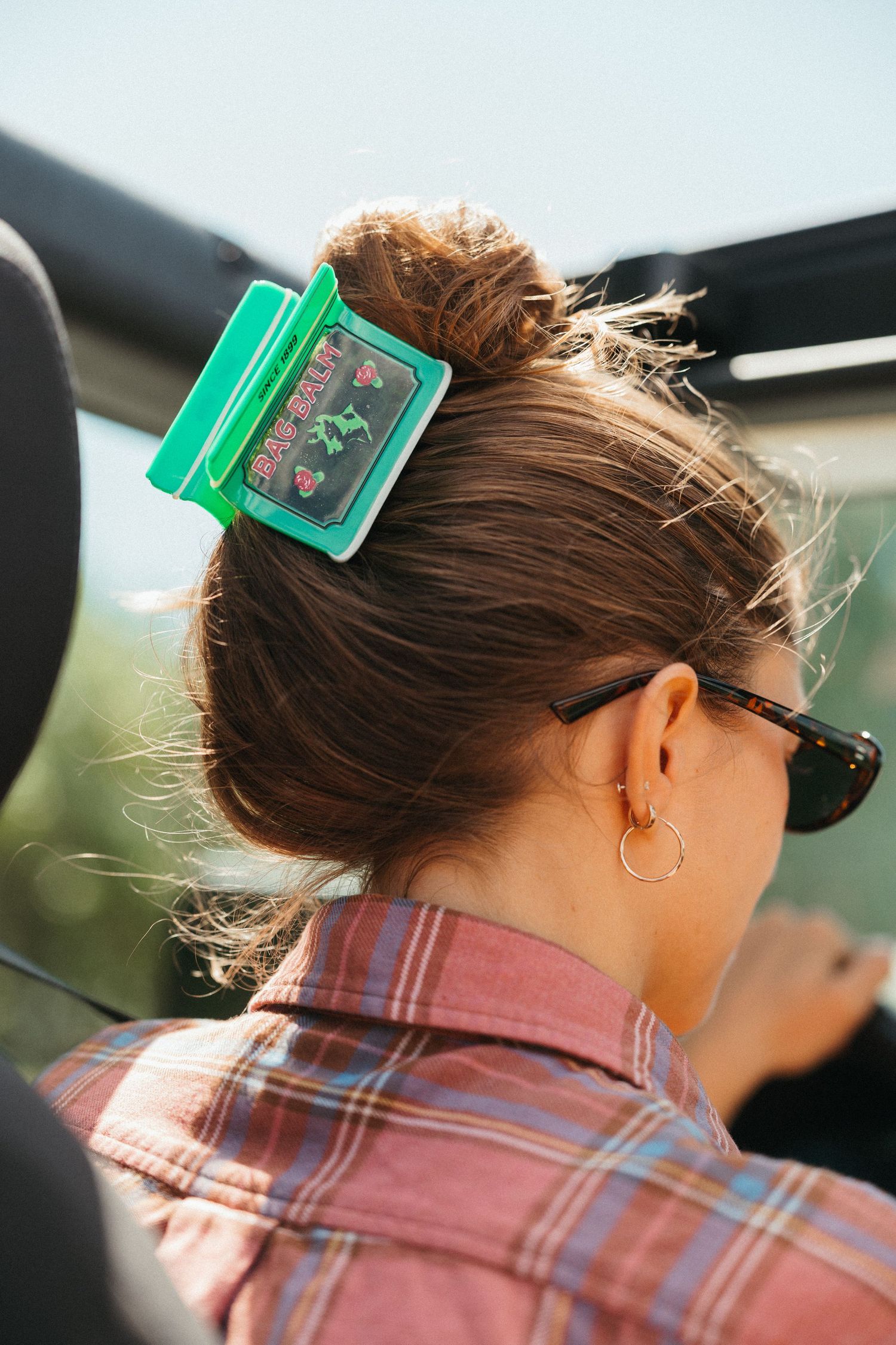 Back view of woman with green Bag Balm hair clip wearing plaid shirt in a car.