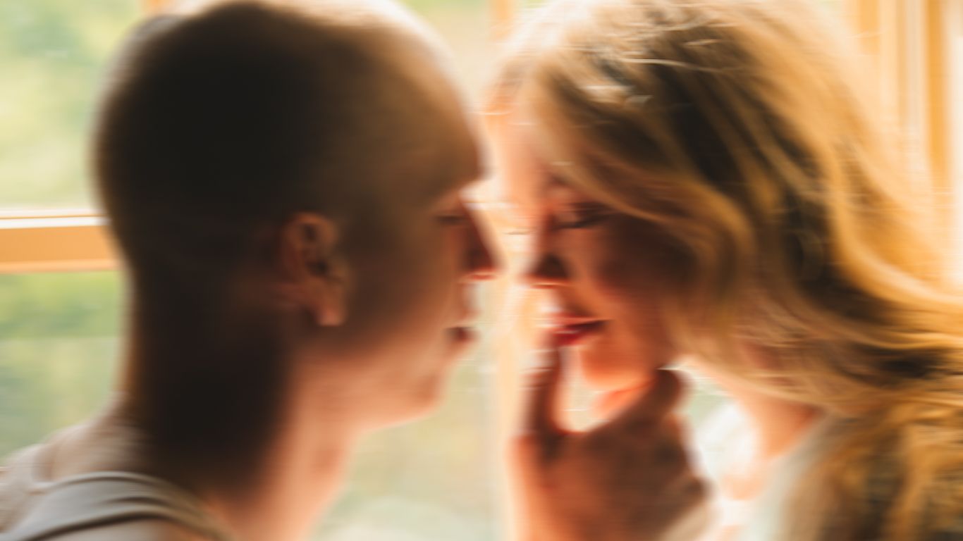 A soft-focus close-up of a couple nearly kissing, bathed in warm natural window light.