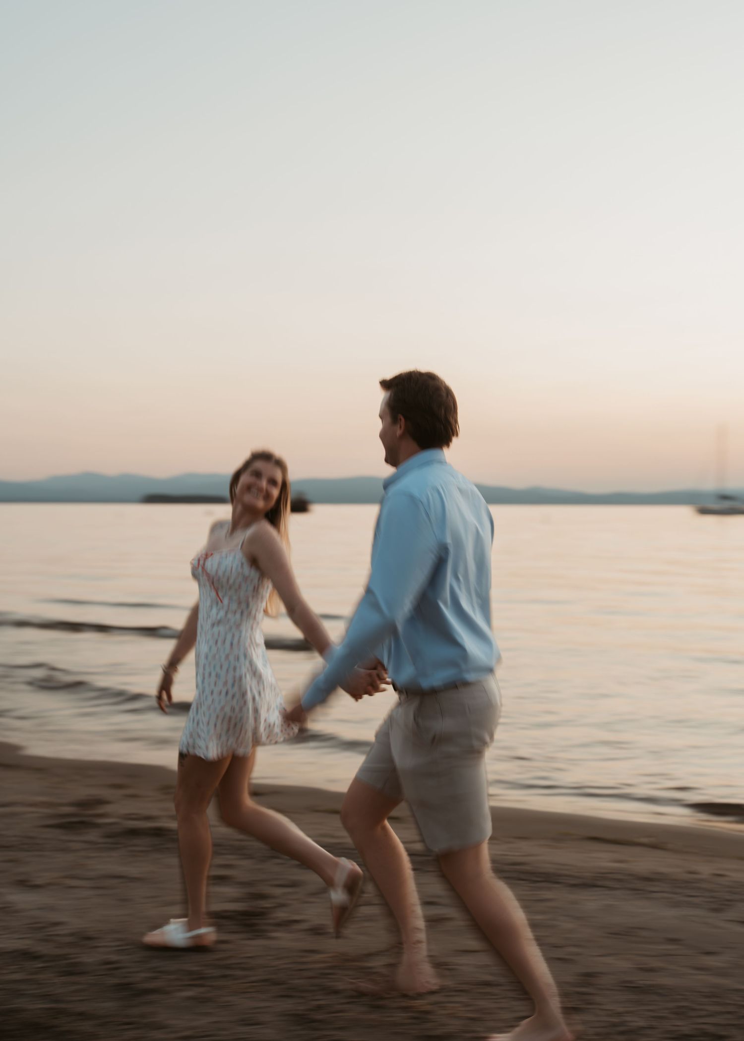 Couple holding hands and dancing playfully on a sandy beach at sunset.