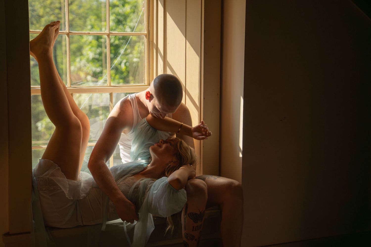 Couple sharing an intimate moment by a sunlit window with warm golden light.