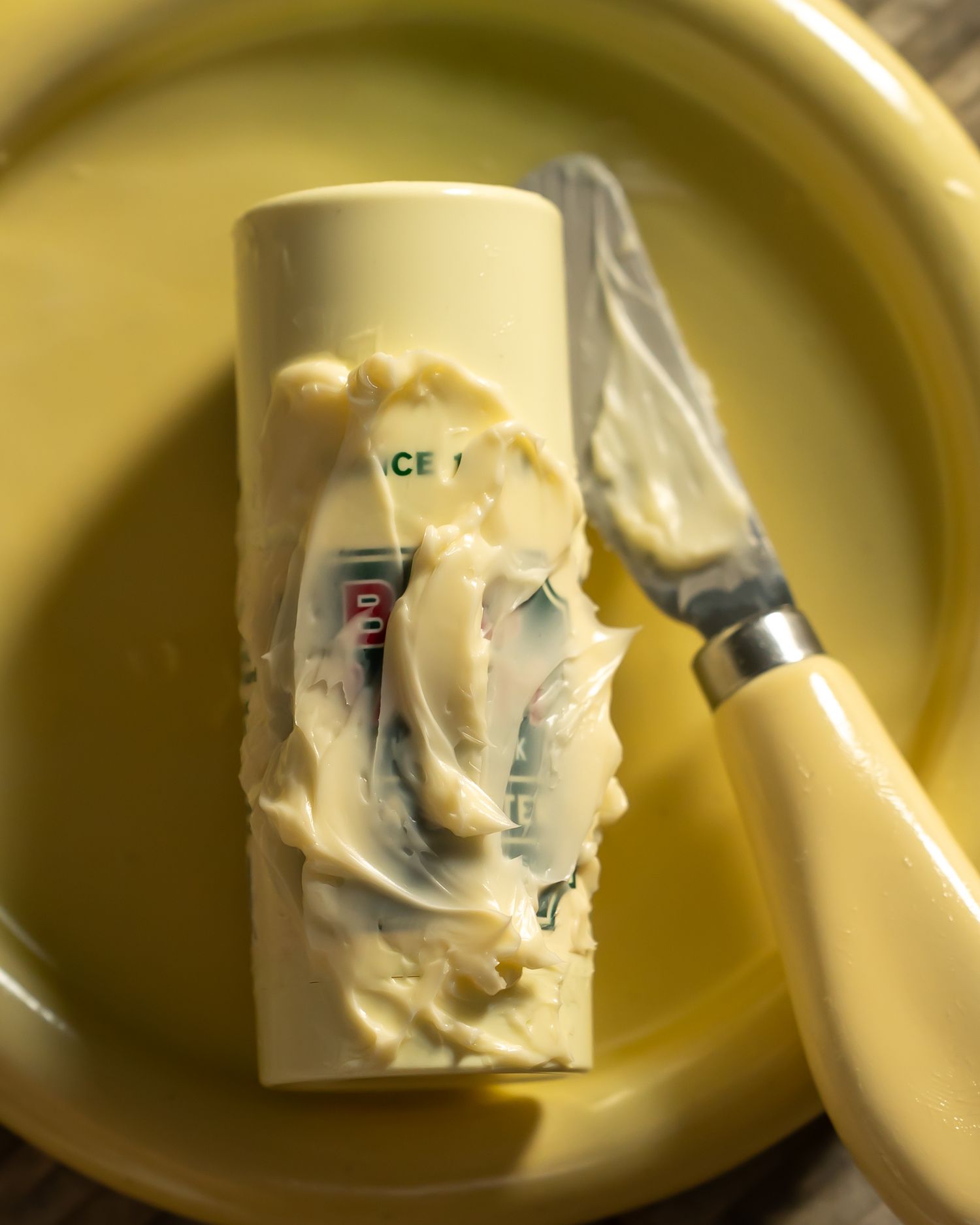 Used Bag Balm moisturizer stick on yellow plate with spreading knife.