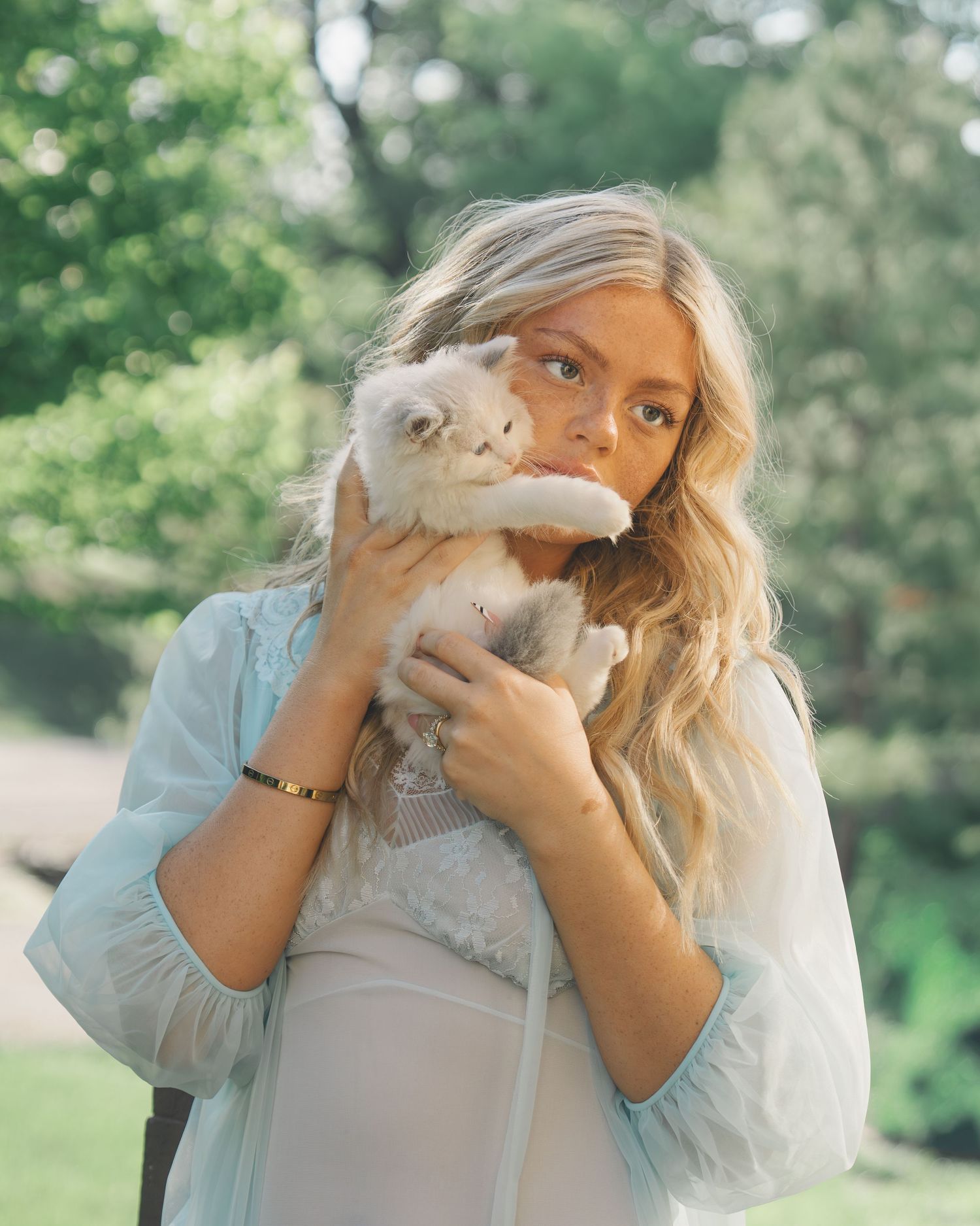 Young blonde woman holding a fluffy white rabbit up to her face in a lush green garden.