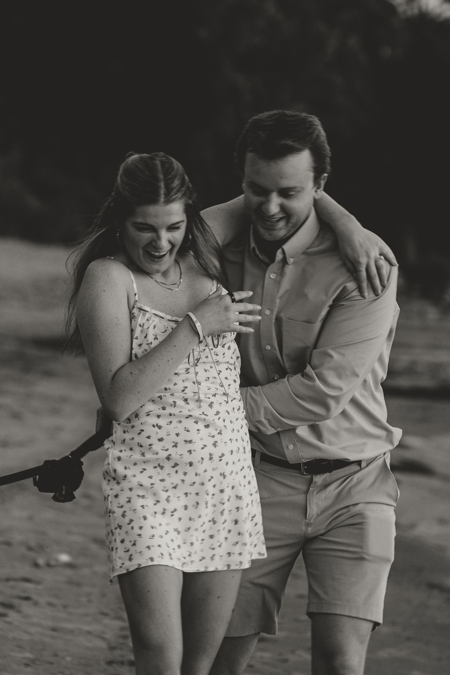 Happy couple laughing and walking together on a beach in black and white photo.