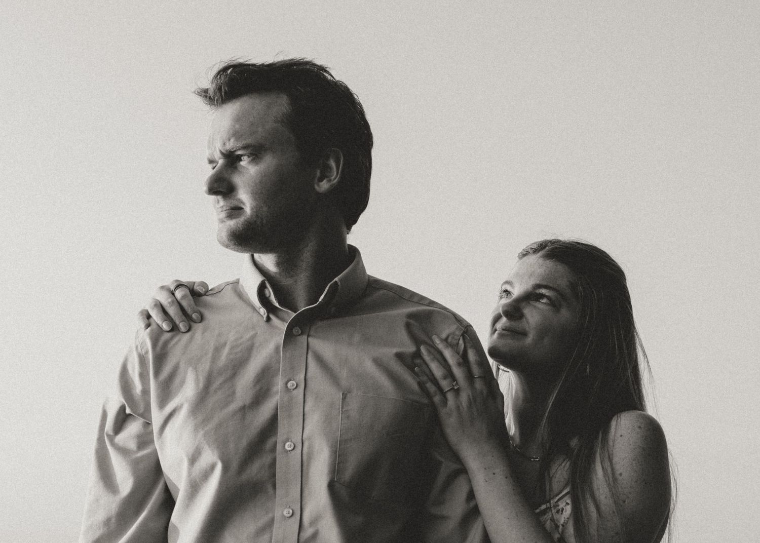 Black and white photo of a couple, woman resting hand on man's shoulder as he gazes away.