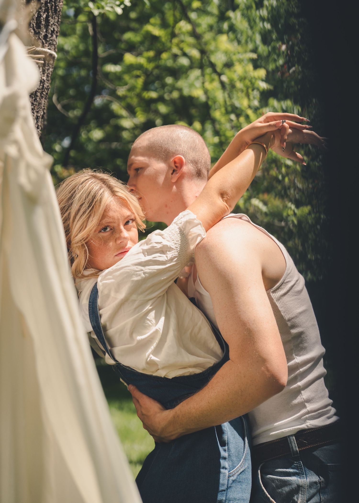 Romantic couple embracing and kissing near a tree in a sunlit outdoor setting.
