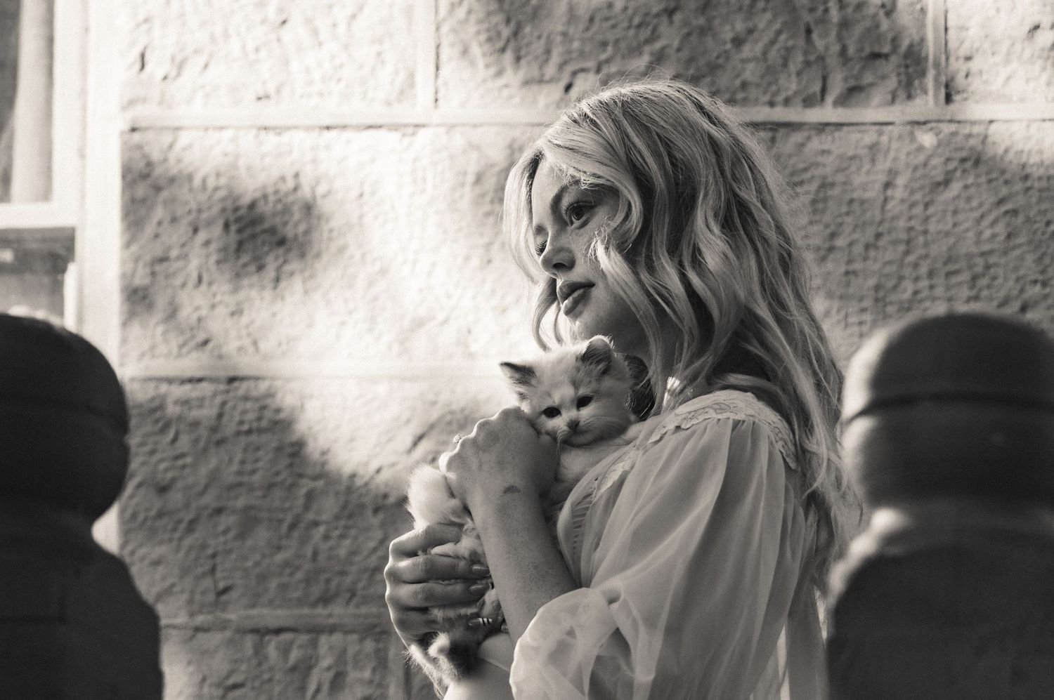 Black and white photo of a blonde woman holding a small white kitten outdoors.