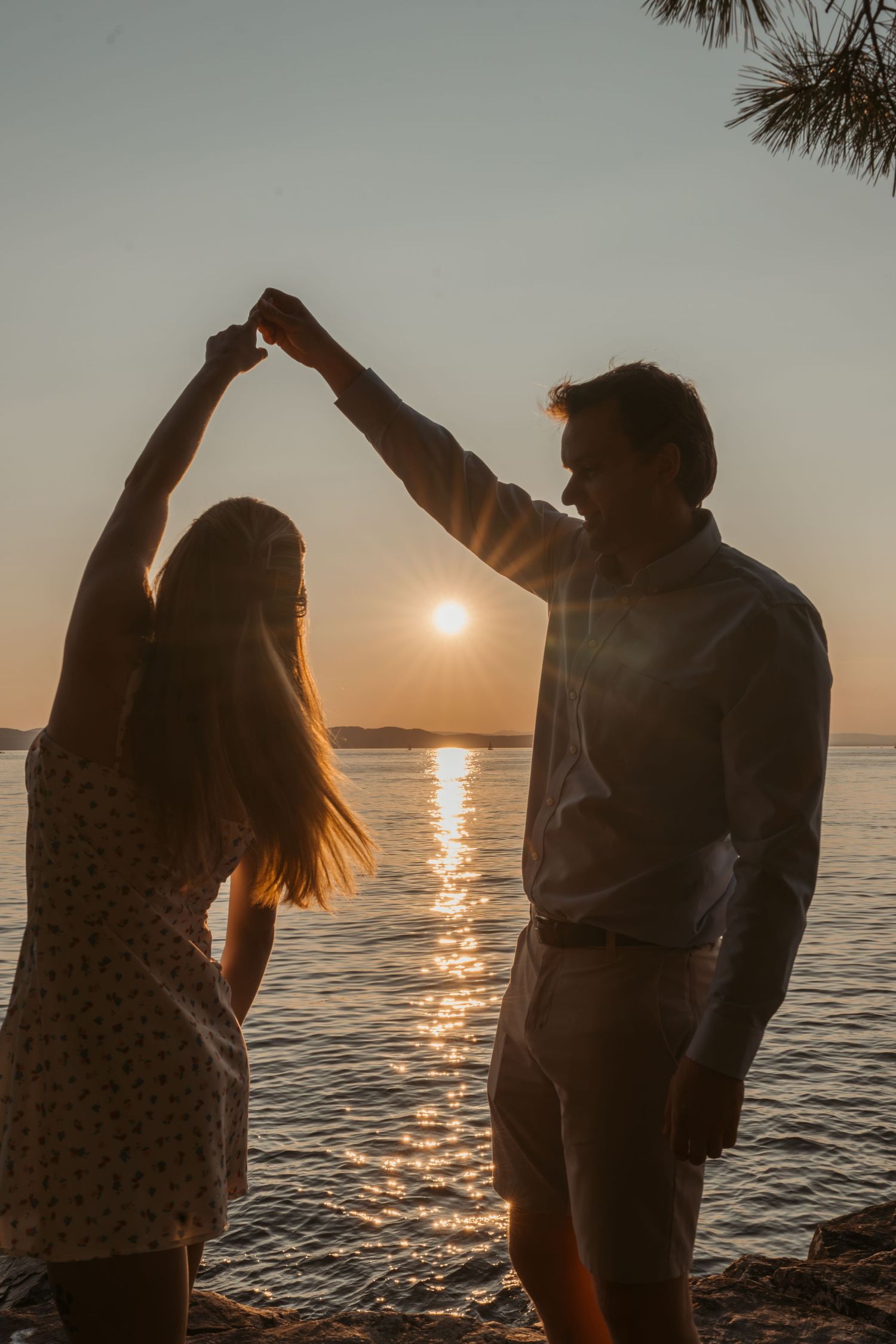 Couple dancing and holding hands at sunset by the ocean with warm golden light.