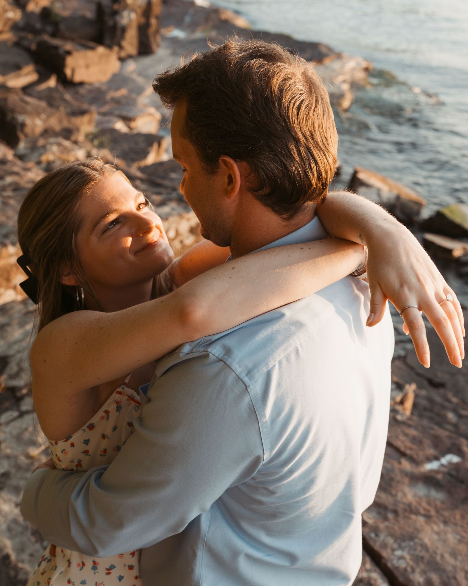 Couple sharing a tender embrace on rocky shore during golden hour sunset.