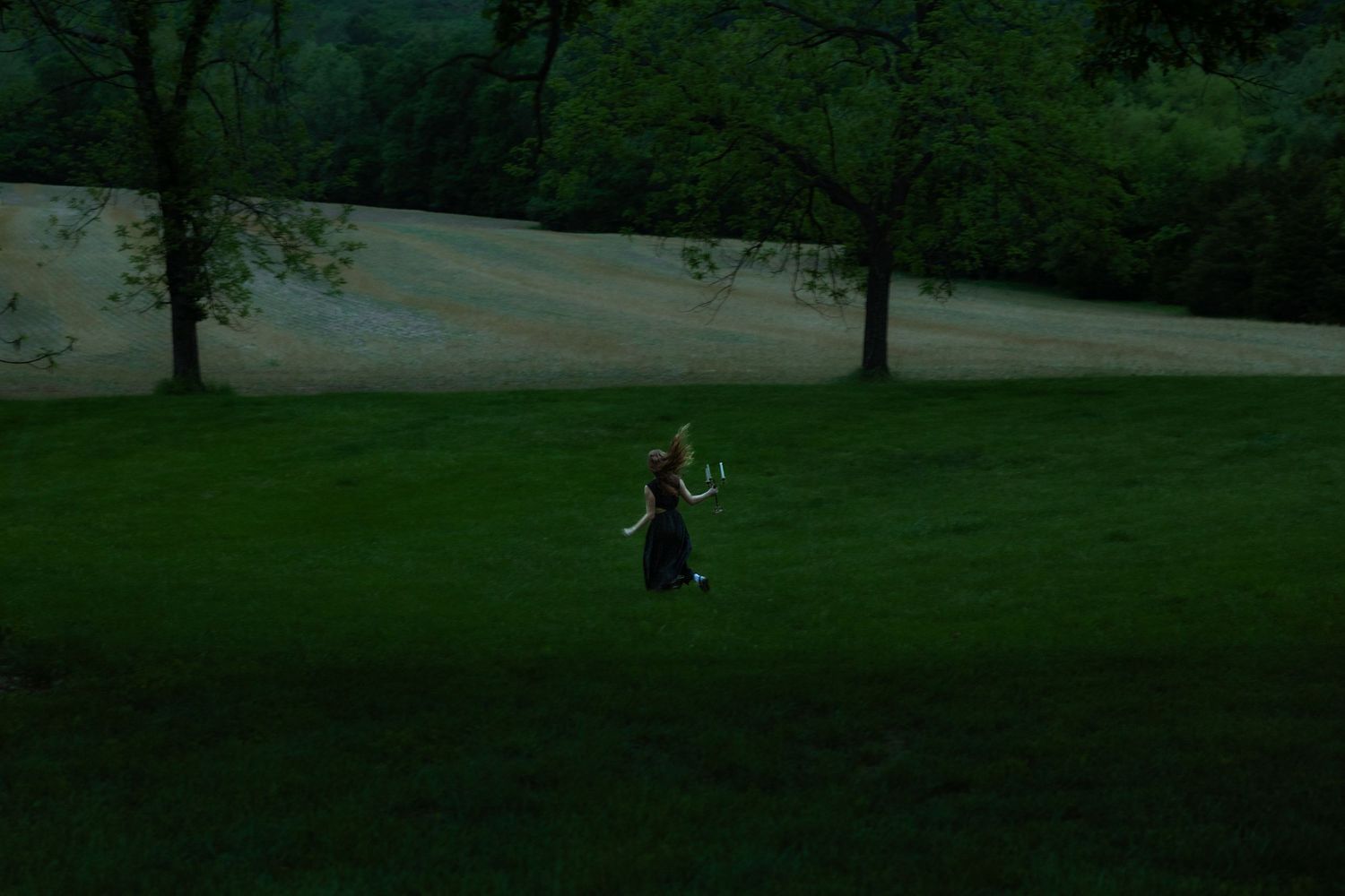 Person walking alone across a lush green lawn at dusk near trees.