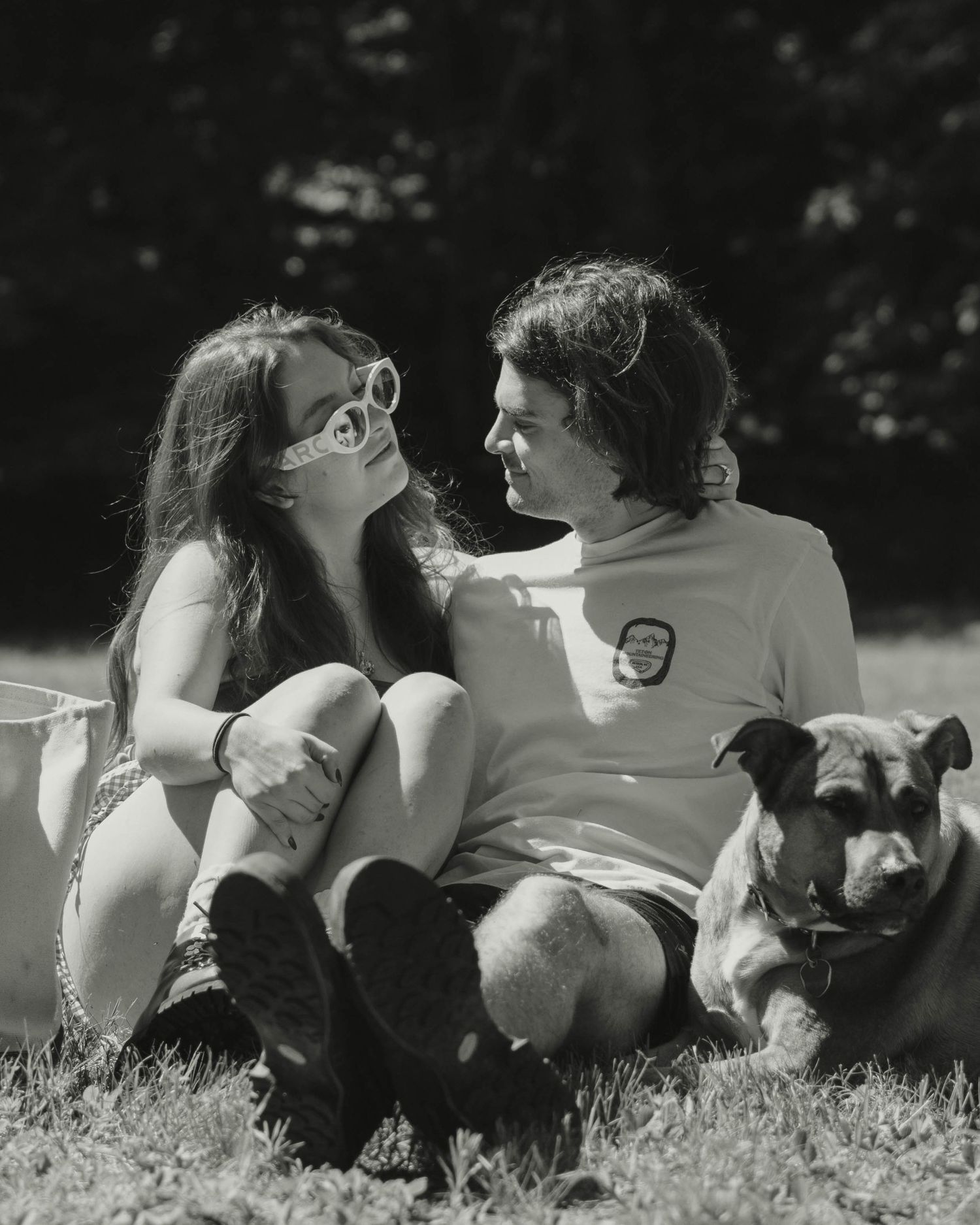 Black and white photo of a couple sitting on grass with their dog outdoors.