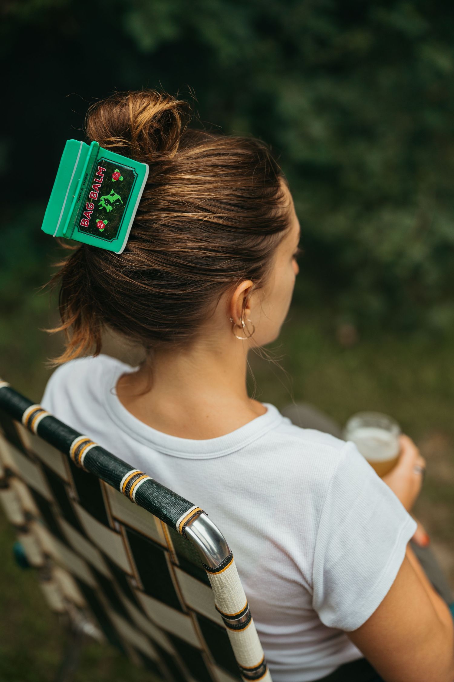 Back view of woman with green Bag Balm hair clip sitting in a chair outdoors.