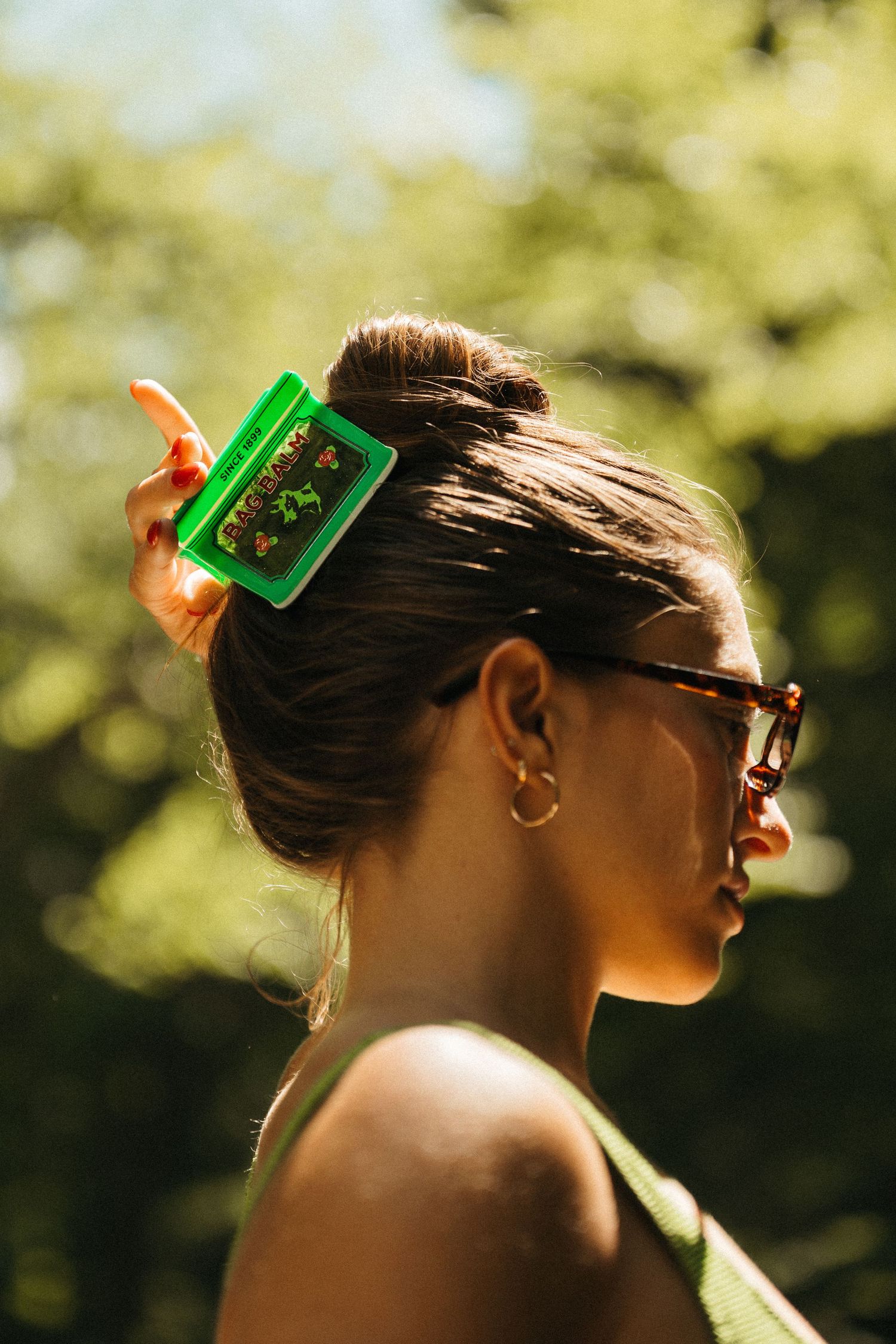 Close-up profile of a woman wearing a green hair clip and tortoise shell sunglasses outdoors.