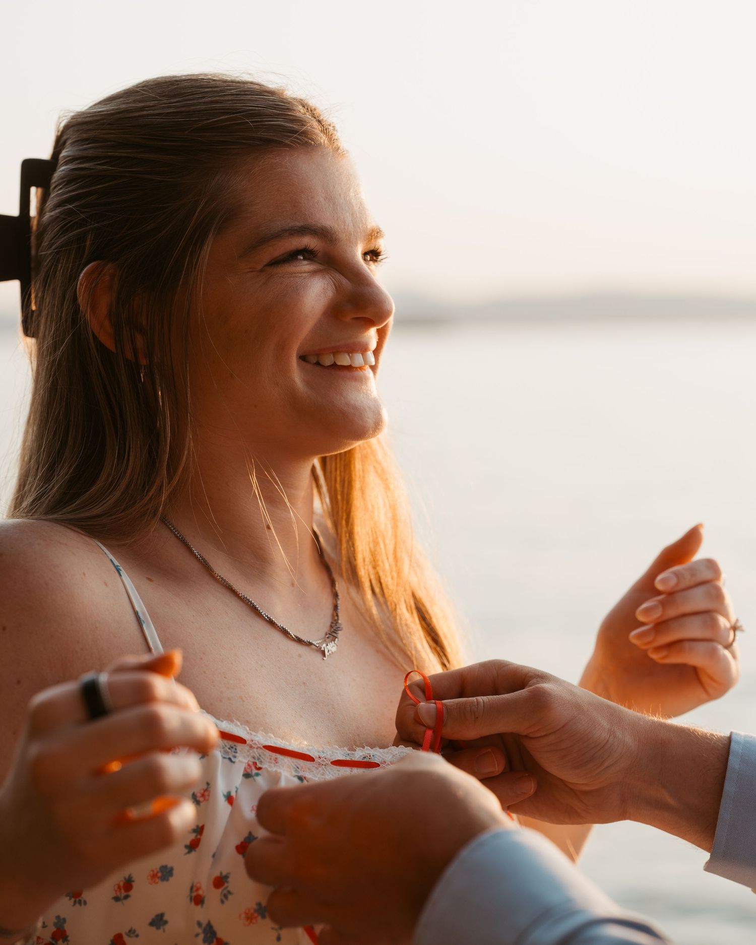 Smiling young woman having her dress bow tied at sunset.