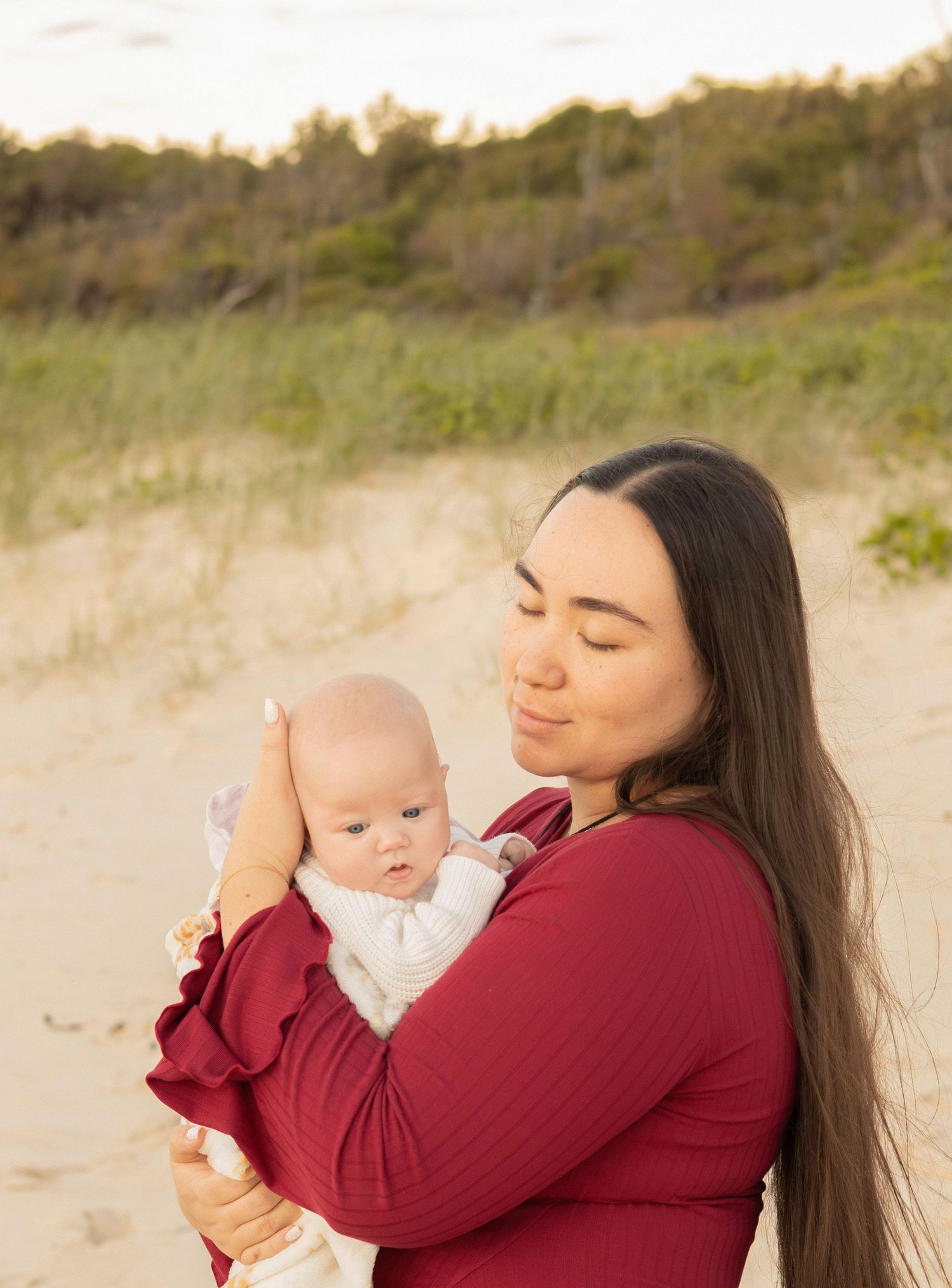 Mother cradling newborn baby on Brisbane beach during golden hour family photography session