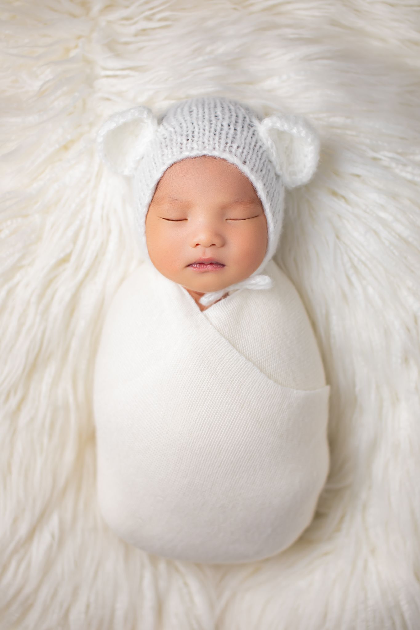 Newborn baby swaddled in white wrap wearing a knit bear ear hat.