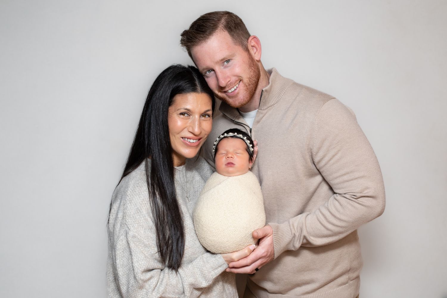 Couple smiling and holding their swaddled newborn baby during a professional studio portrait session.