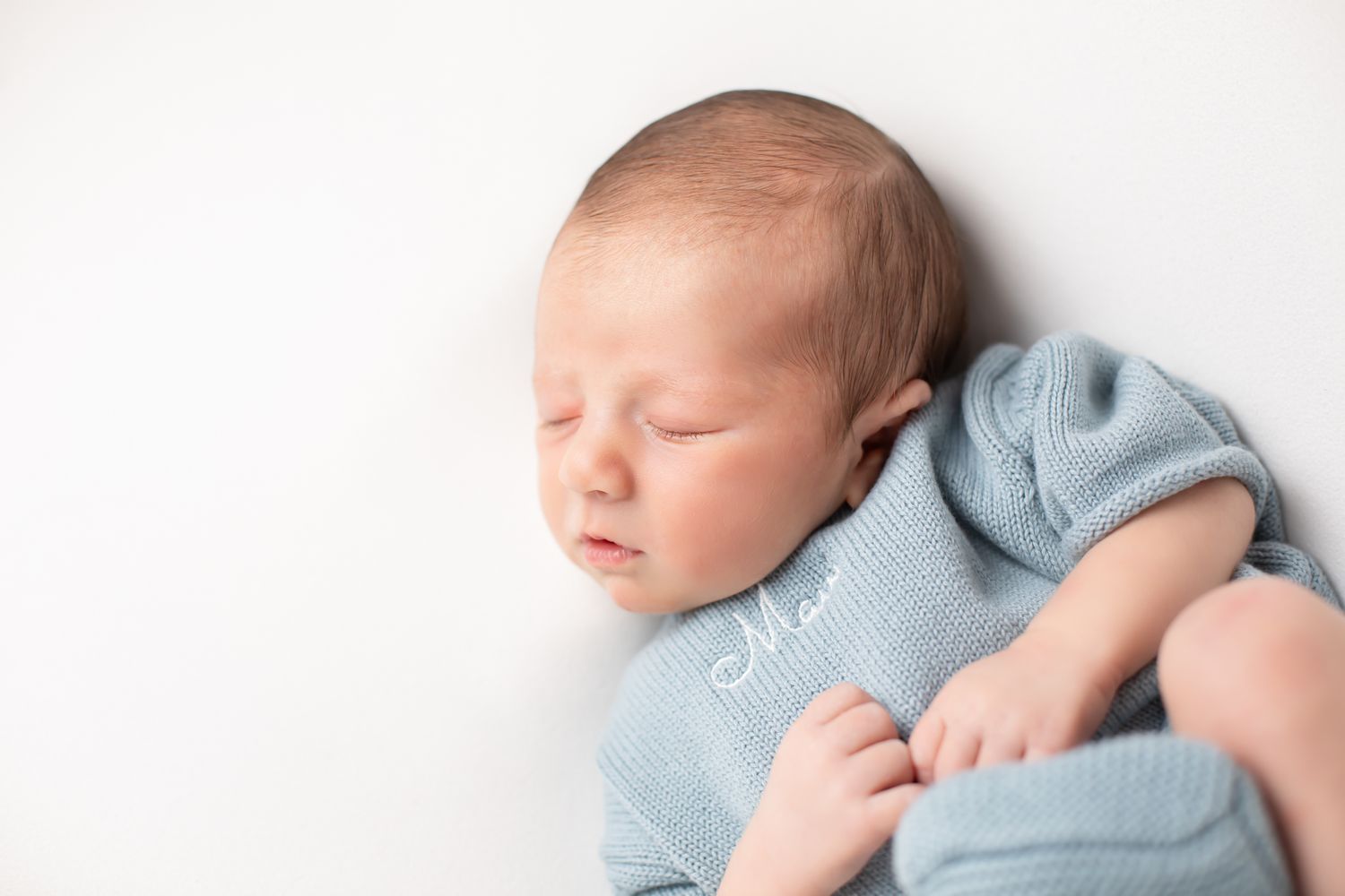 Sleeping newborn baby wrapped in a soft blue knit swaddle on white background.