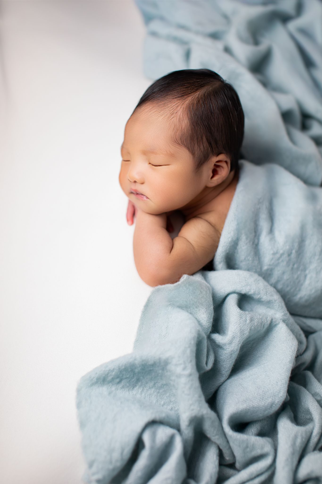 Newborn baby sleeping peacefully wrapped in a soft teal blanket.