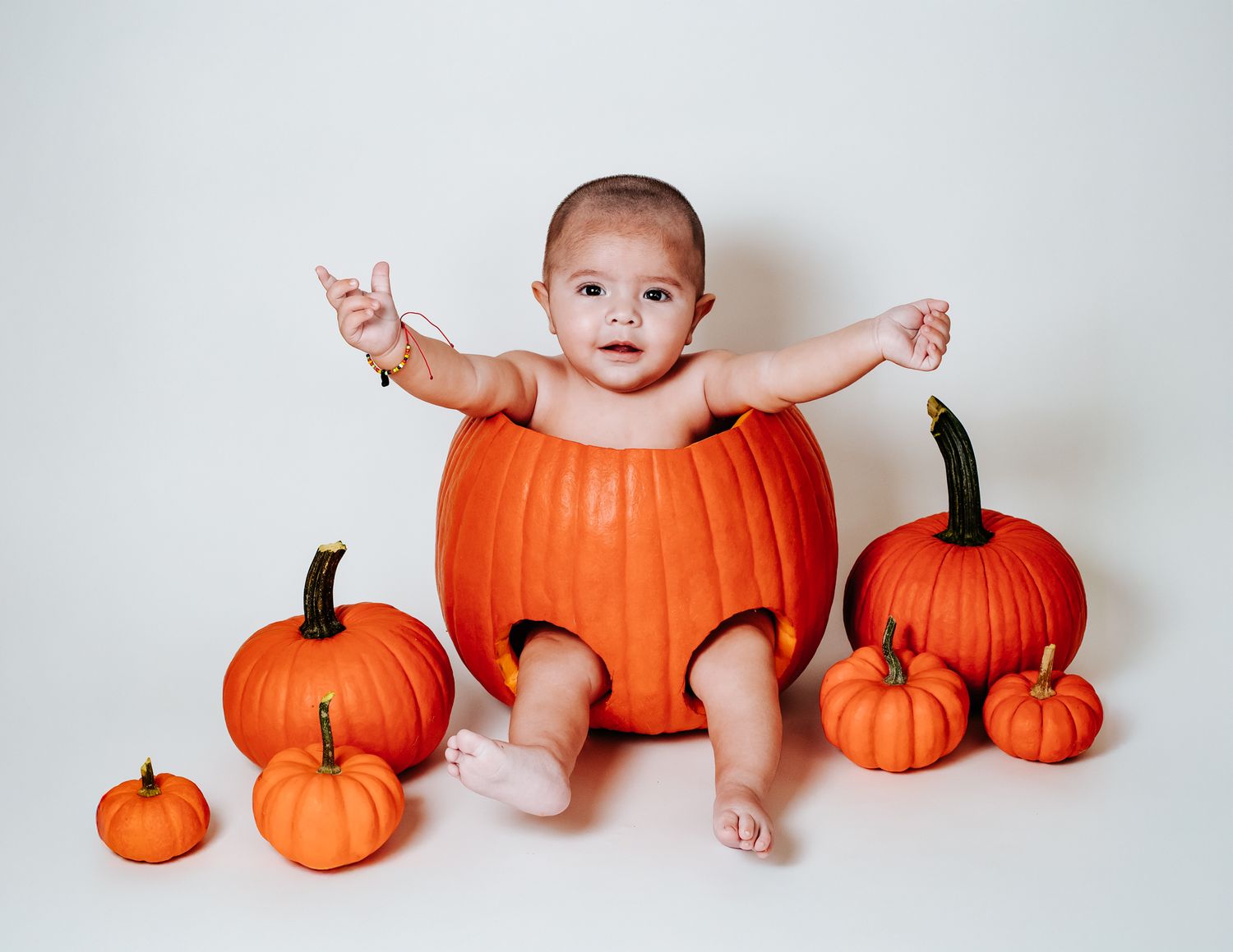 Adorable baby sitting inside a large carved pumpkin surrounded by small pumpkins for Halloween photo.
