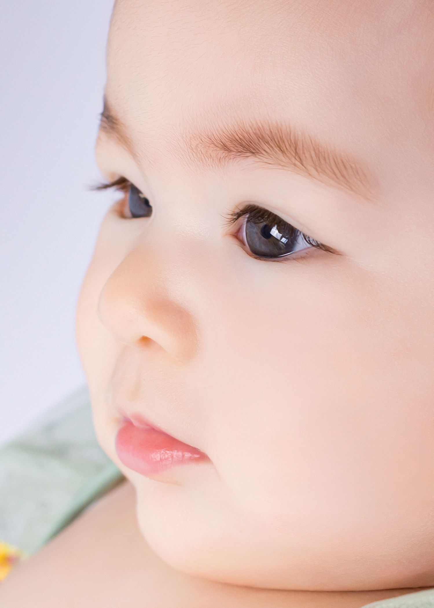 Close-up portrait of an adorable baby with big dark eyes and soft skin looking upward curiously.