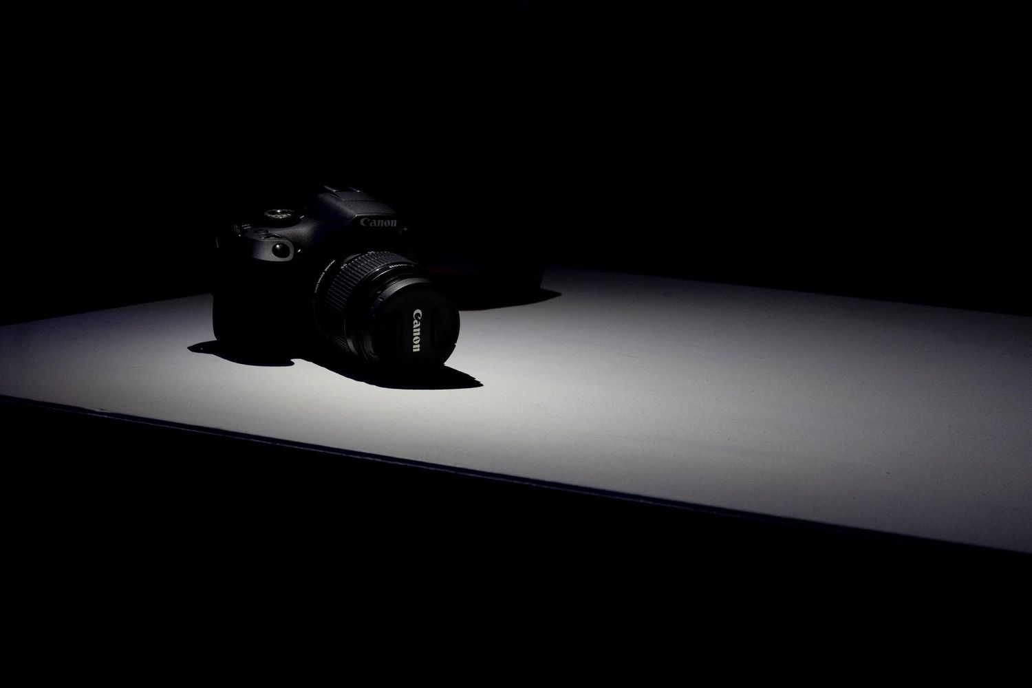 DSLR camera illuminated by spotlight on a dark surface with dramatic low-key lighting.
