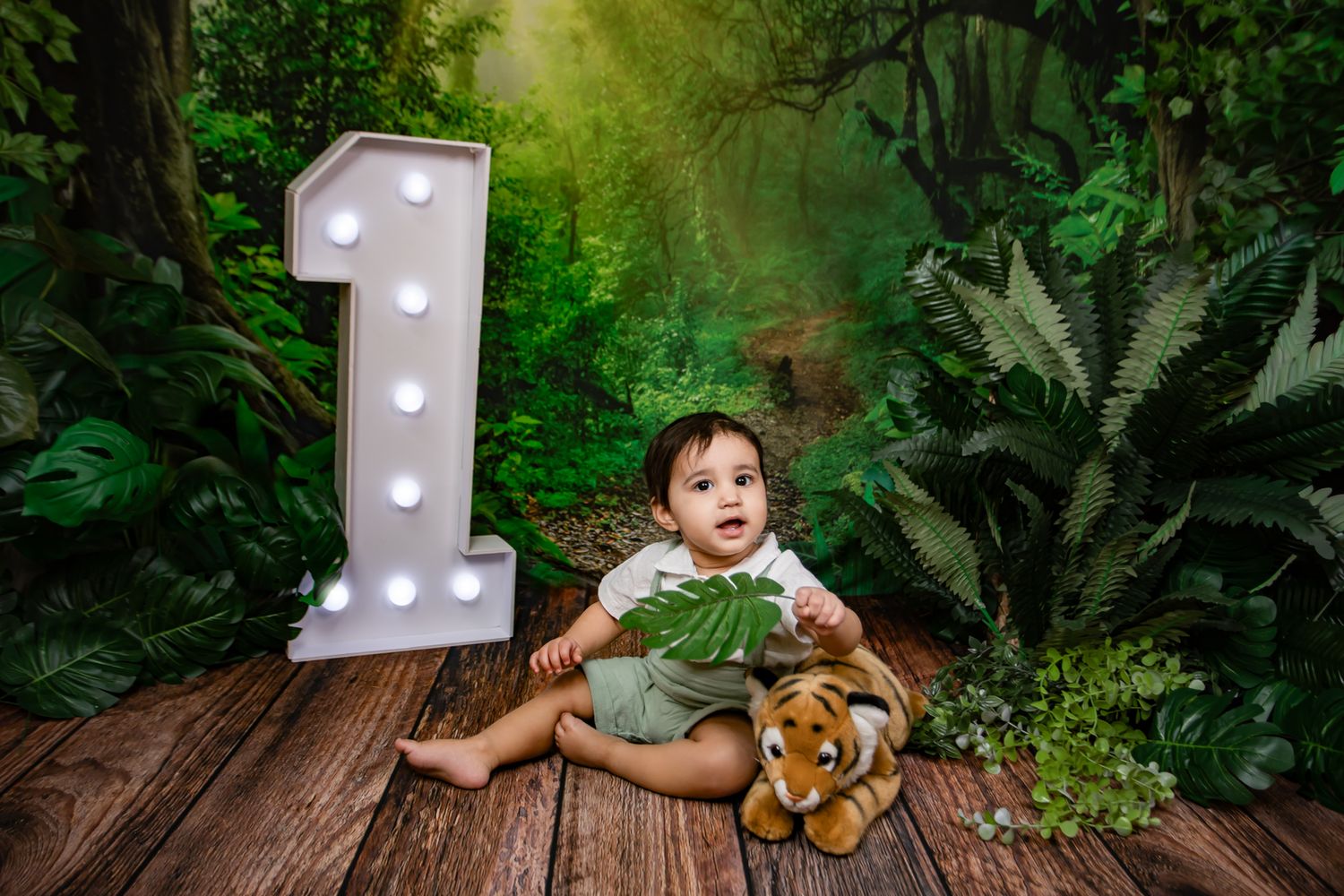 Baby's first birthday photo with jungle theme, light-up number one, and tiger stuffed animal.