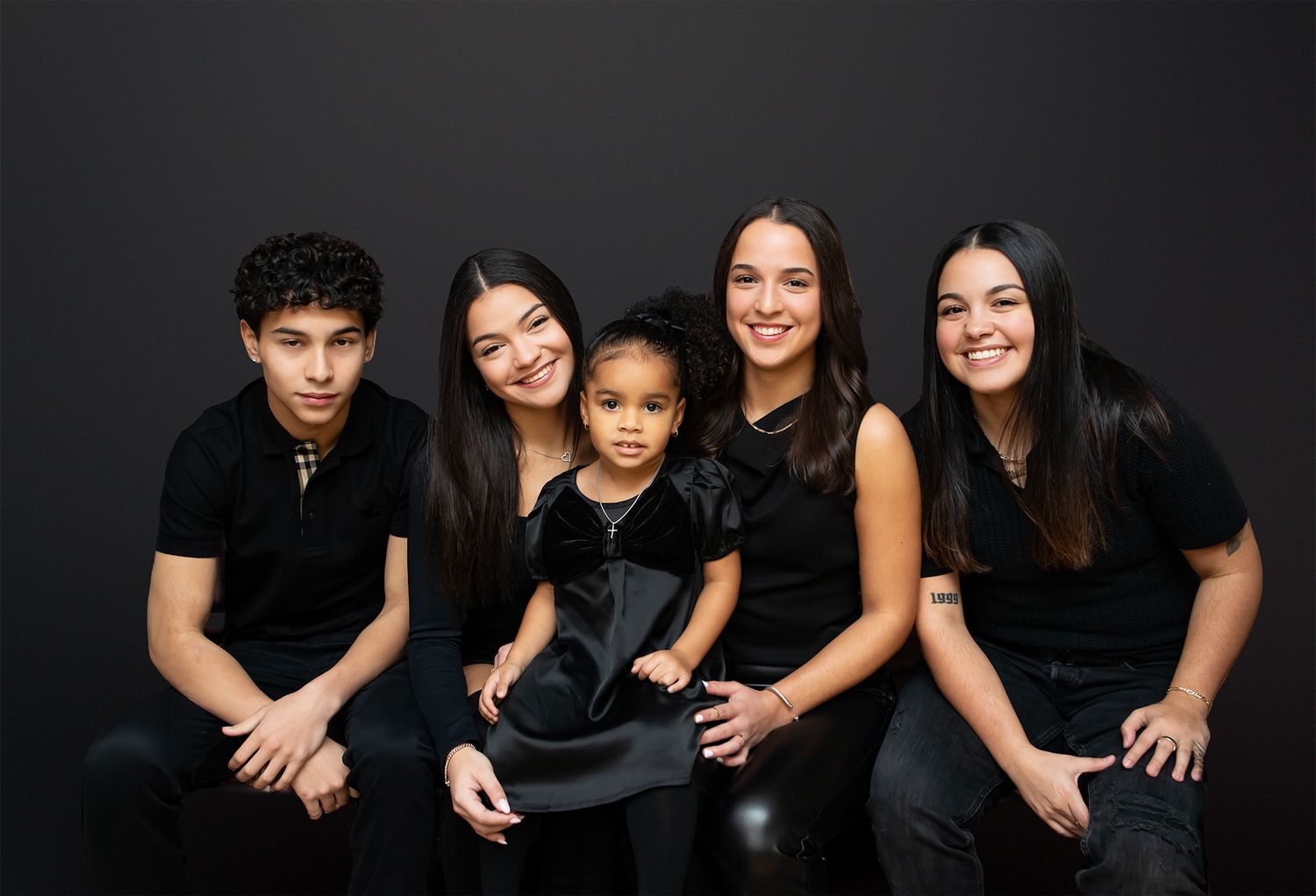 Family of five wearing matching black outfits pose together for a studio portrait on dark background.