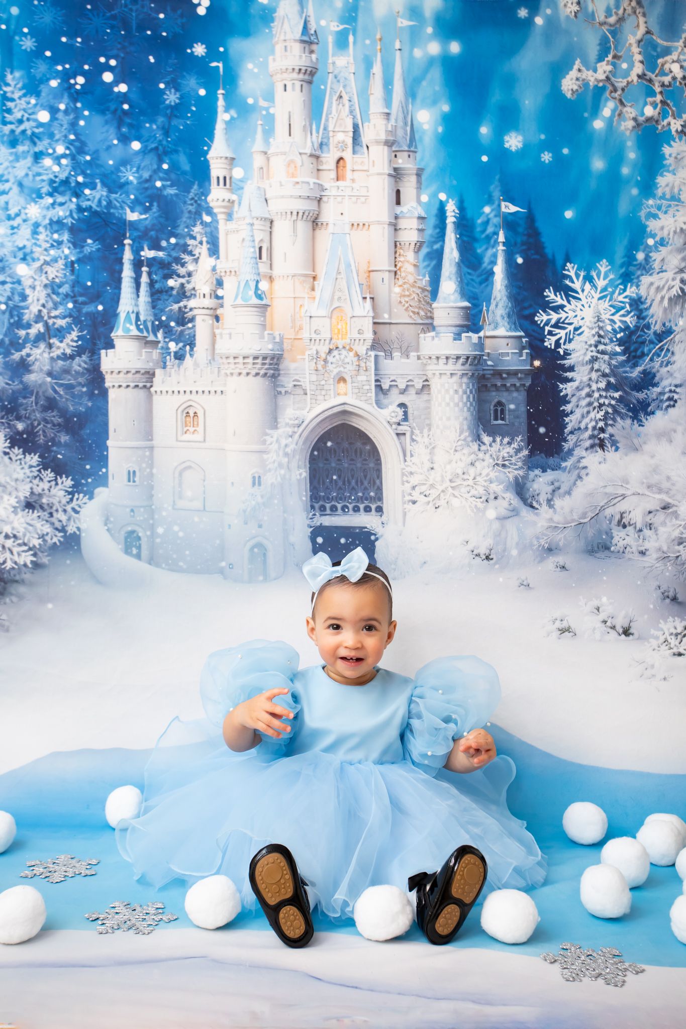 Joyful baby girl in blue puff-sleeve dress laughs before a magical winter castle backdrop.