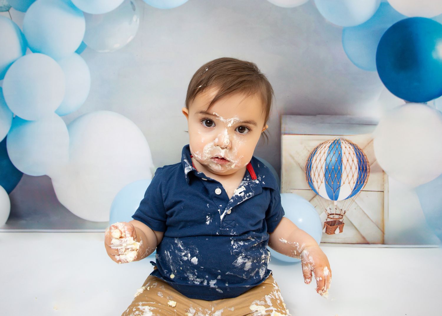 Adorable baby boy with cake smash frosting on face during first birthday photo session.
