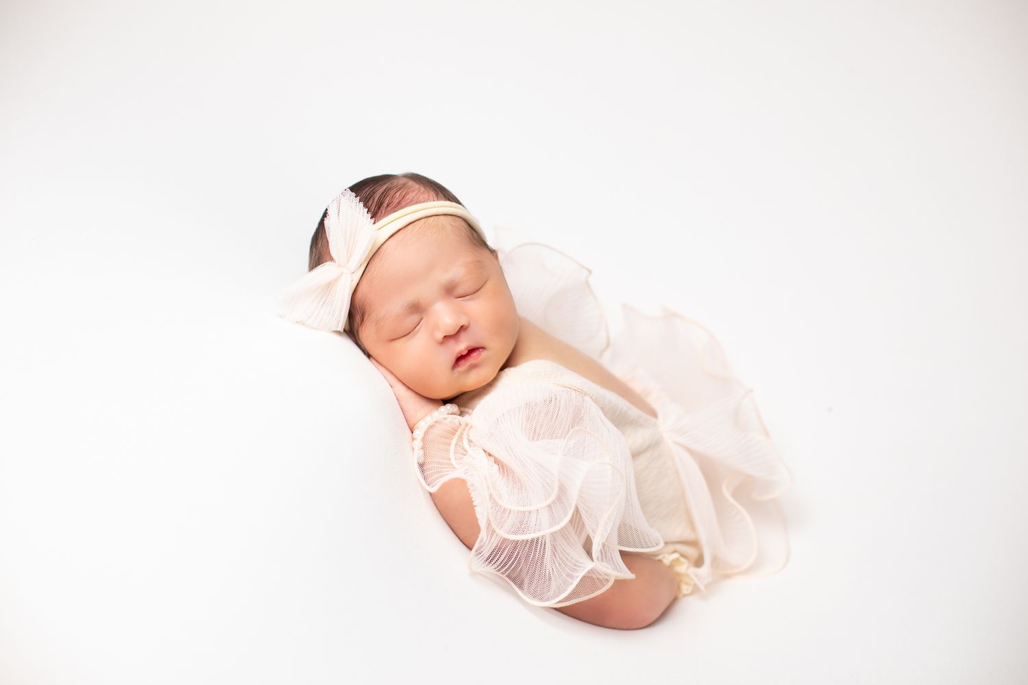Newborn baby girl sleeping peacefully wrapped in a soft peach tulle swaddle with bow headband.