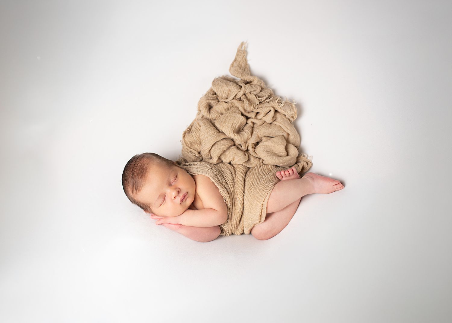 Sleeping newborn baby wrapped in a beige knit blanket on a white background.