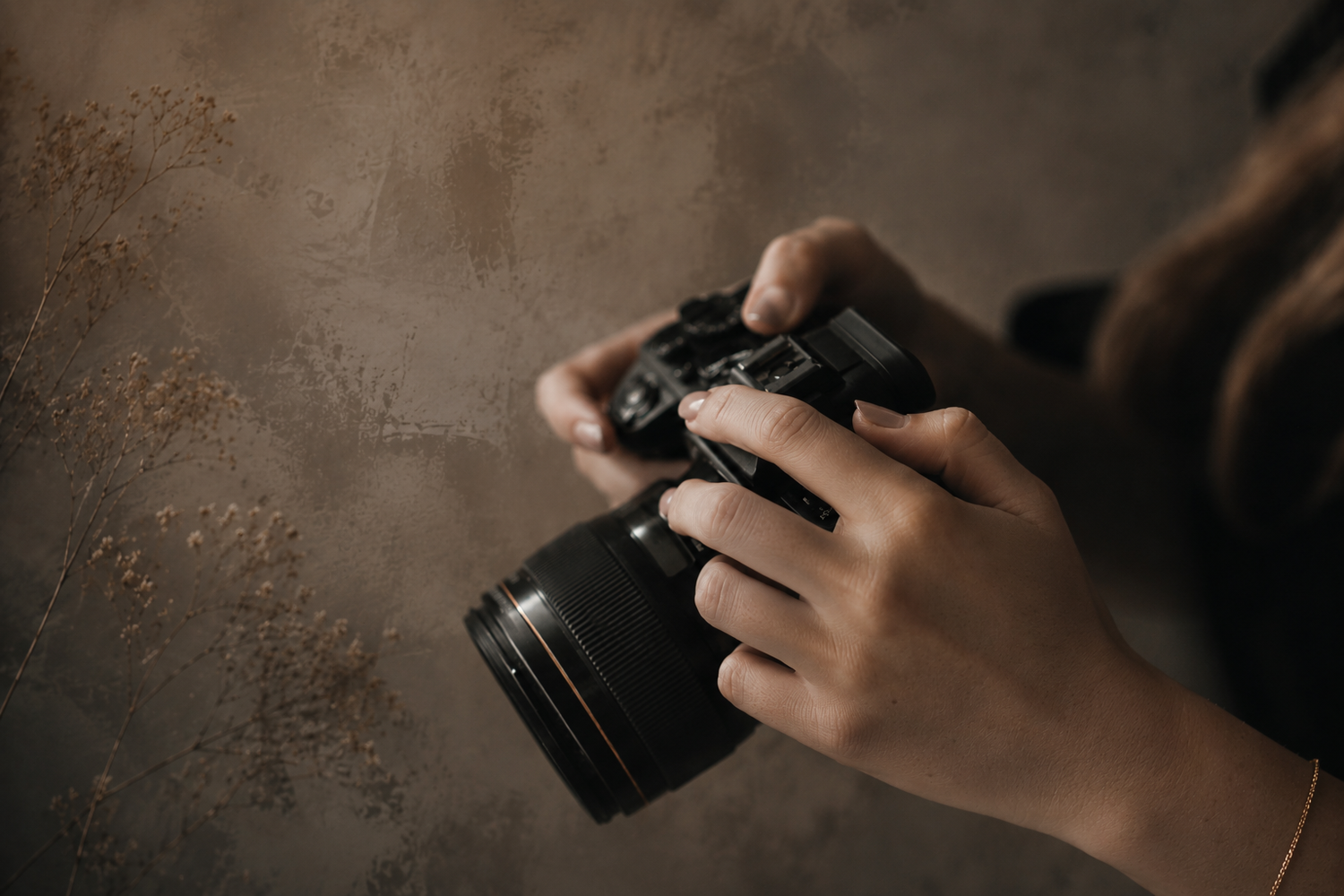 Close-up of hands holding a DSLR camera against a textured brown background.