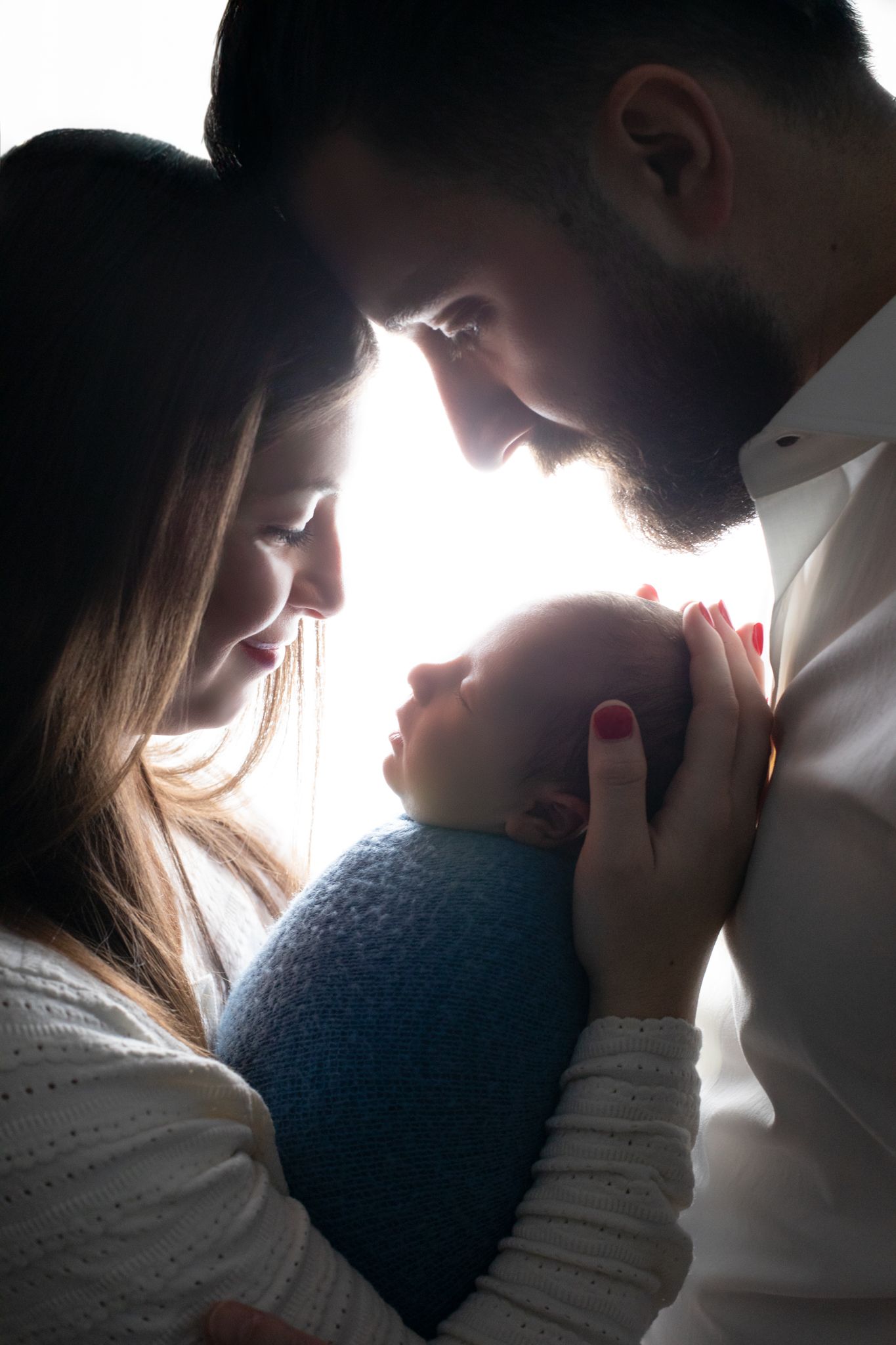 Parents tenderly cradling their sleeping newborn baby in a beautiful backlit silhouette portrait.