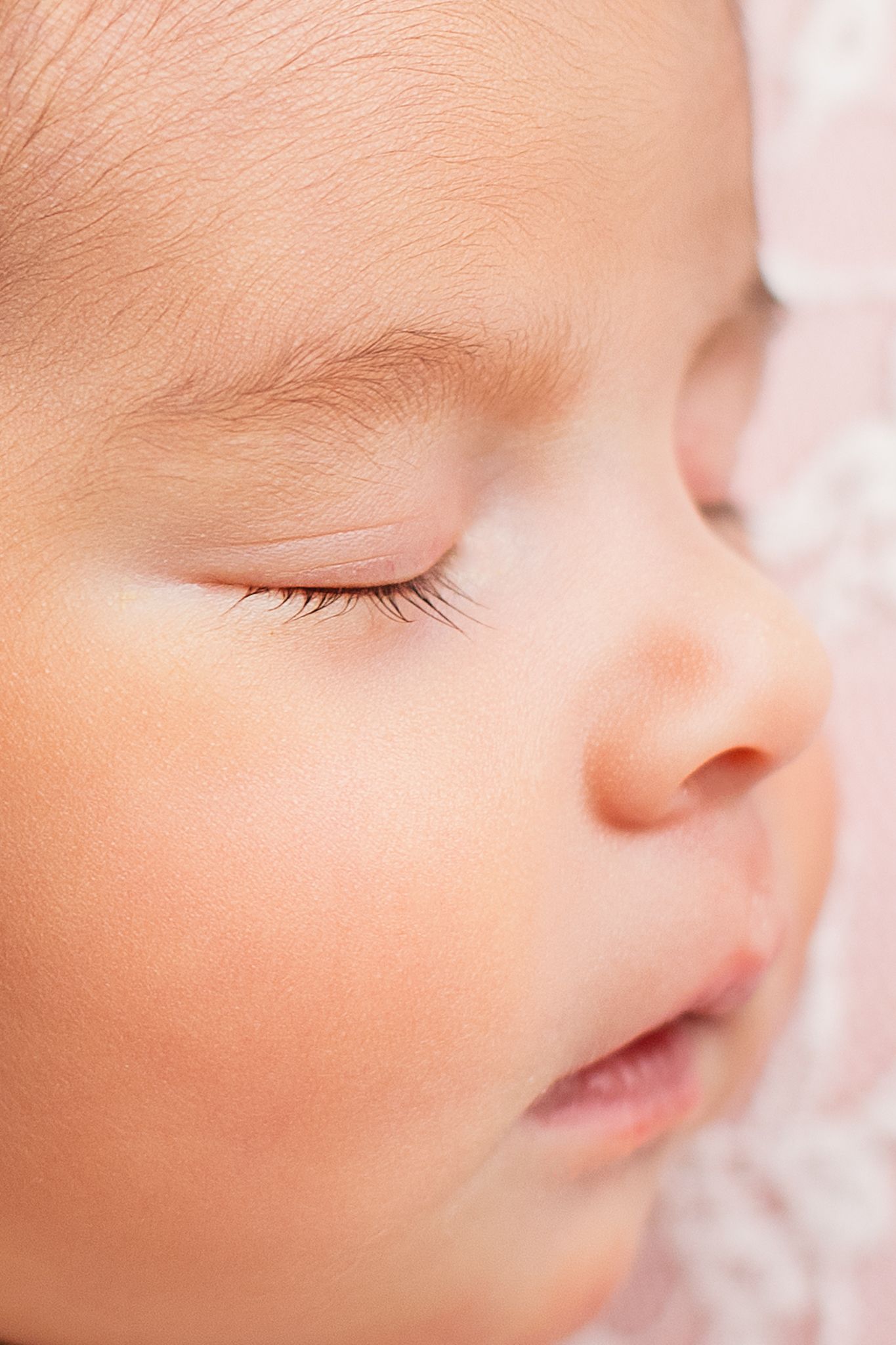 Close-up portrait of a sleeping newborn baby with delicate eyelashes on a soft pink background.