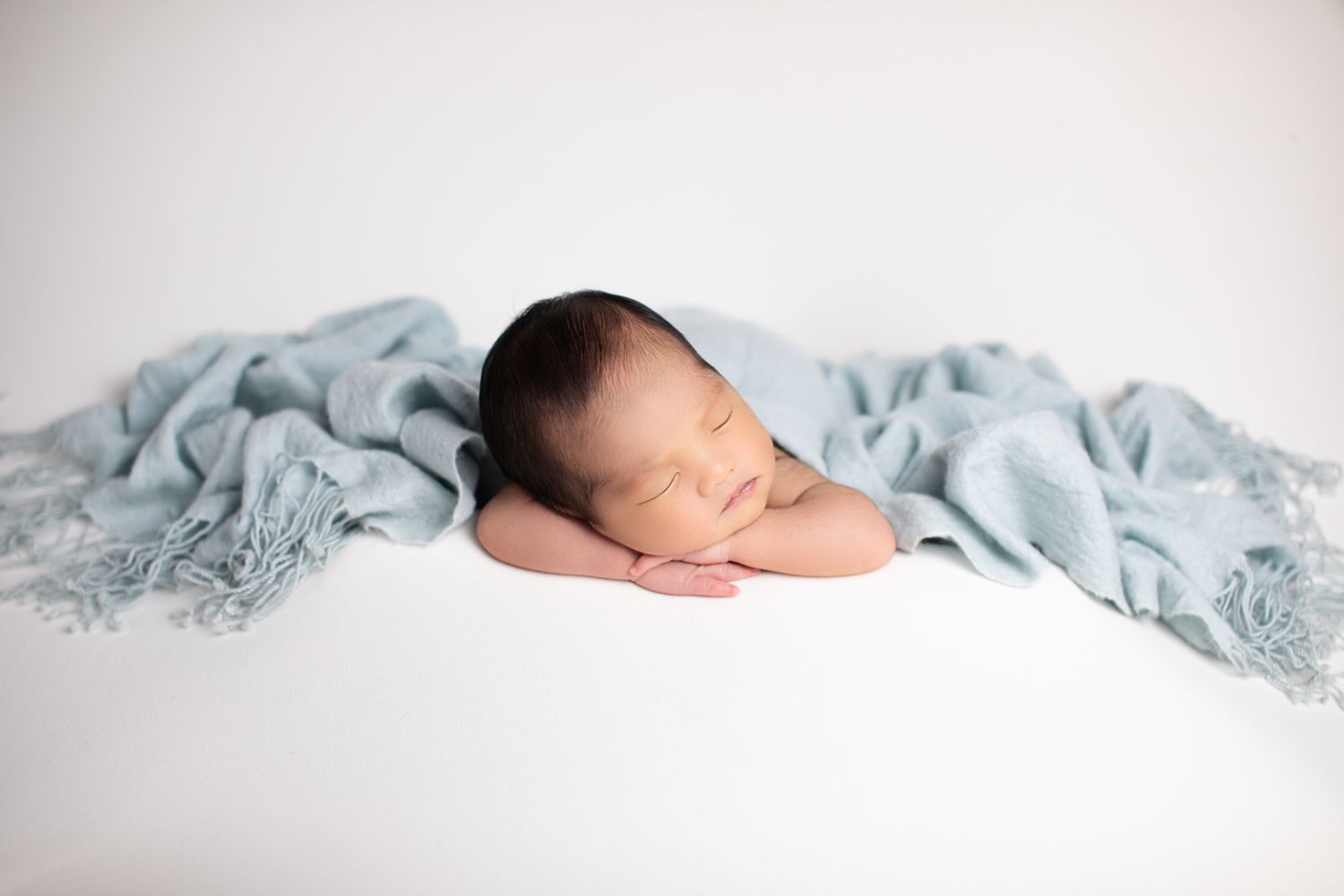 Sleeping newborn baby wrapped in a soft teal blanket on a white surface.