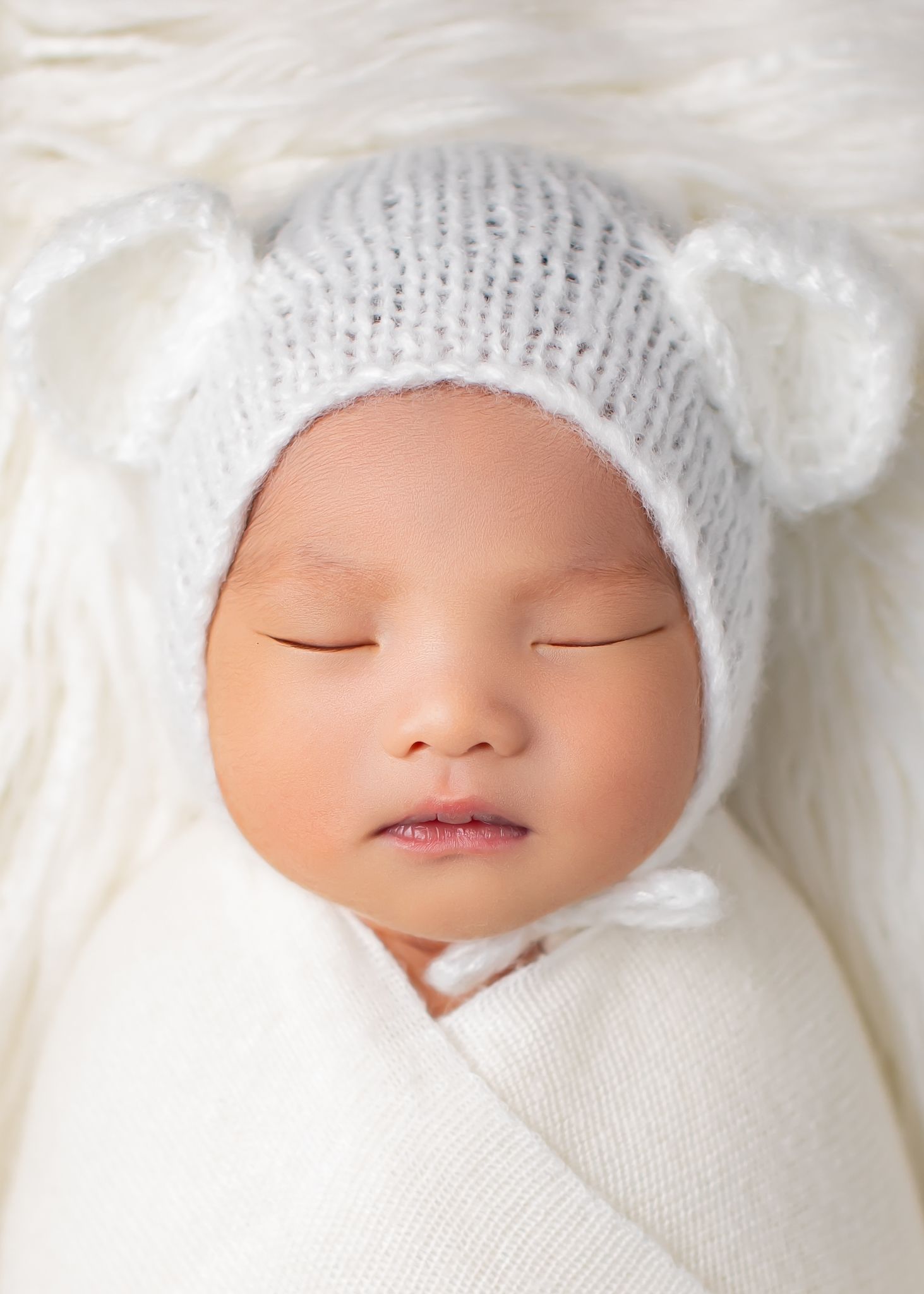 Close-up of newborn baby in white swaddle wearing a gray bear ear hat.