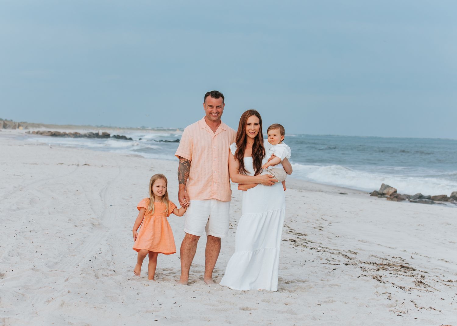 Beautiful family of four posing together on sandy beach with ocean in background at golden hour.