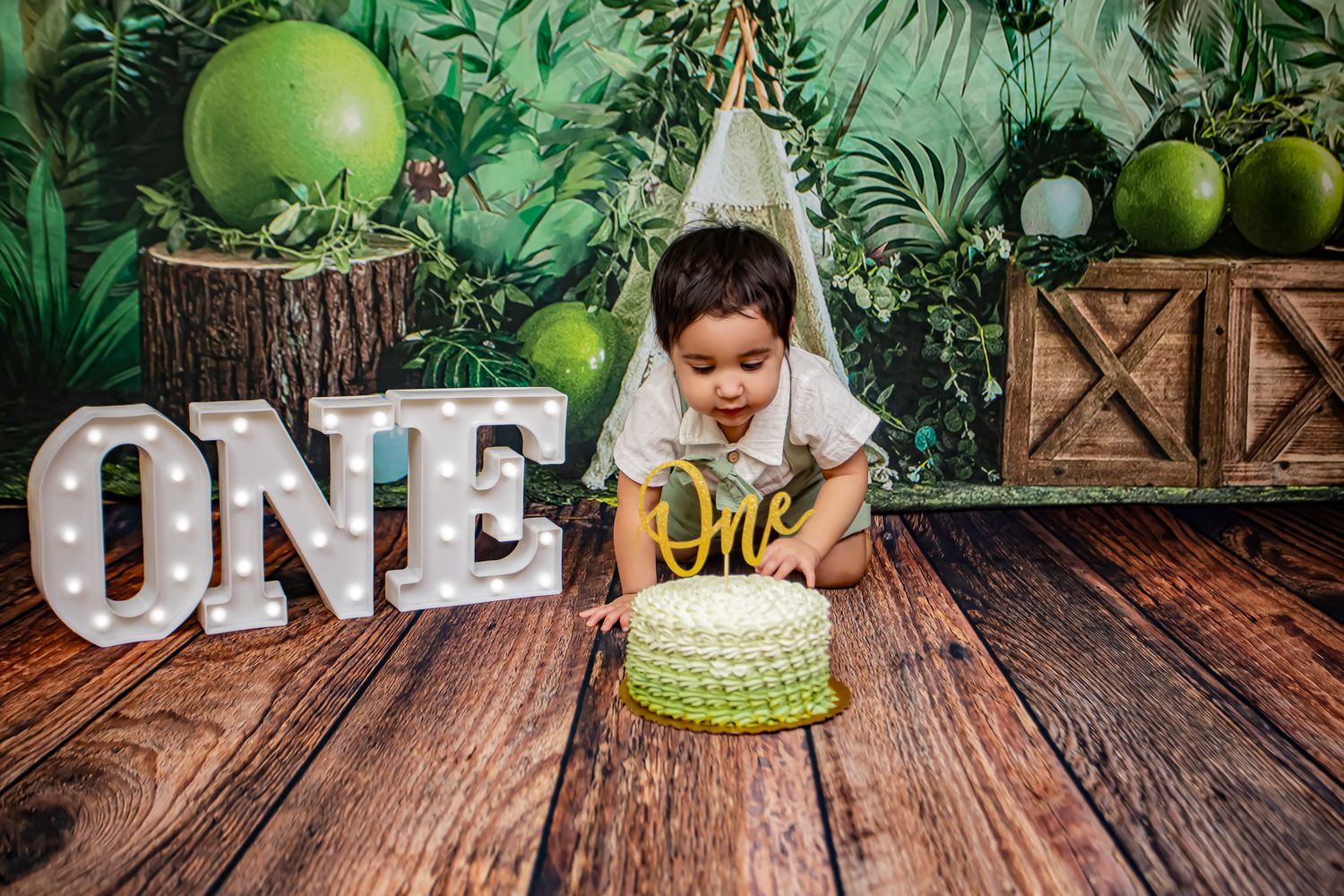 Toddler boy smashes green ombre first birthday cake in a jungle-themed photo session.