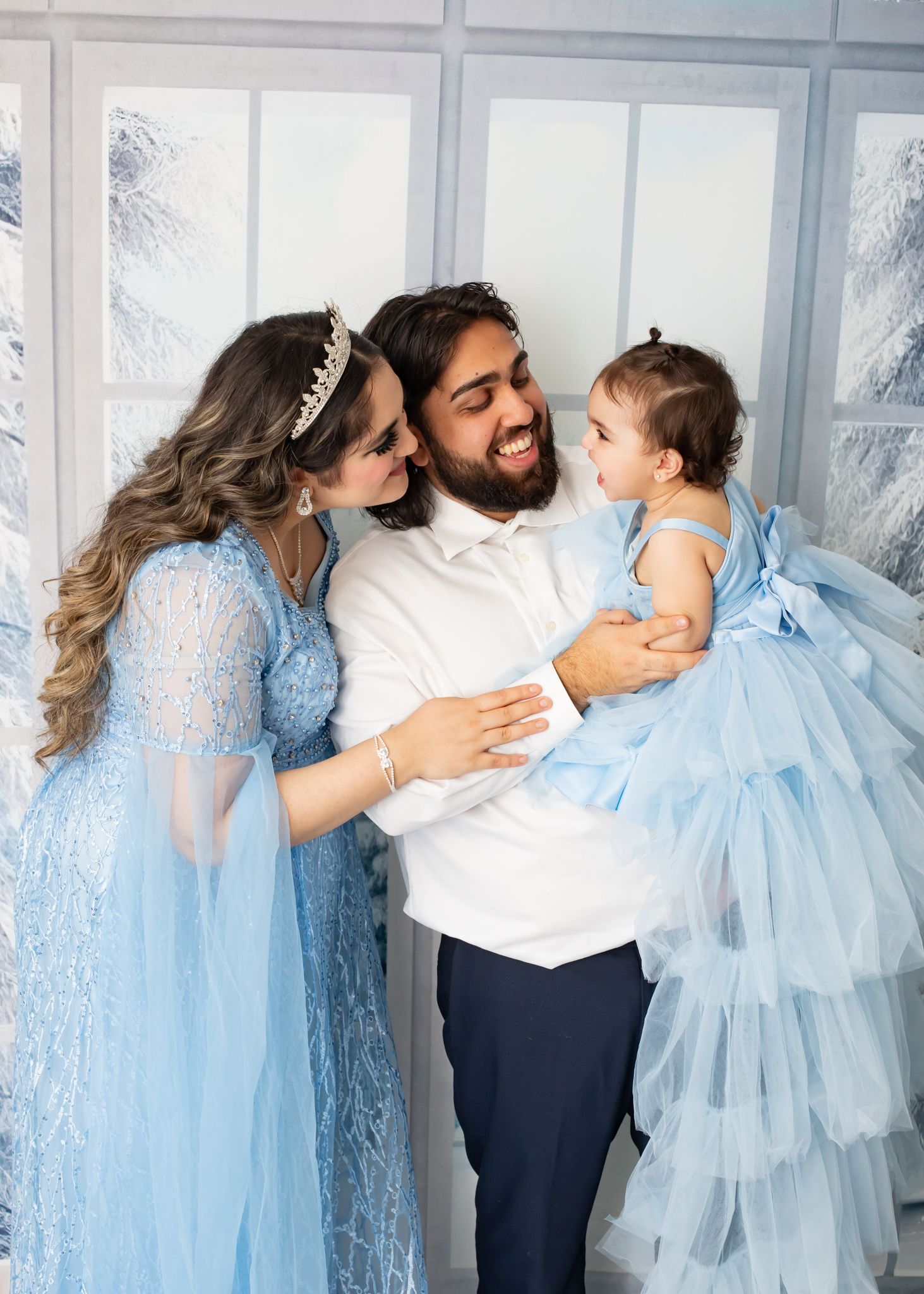Happy family with parents in blue outfits laughing with baby girl in blue tulle dress.