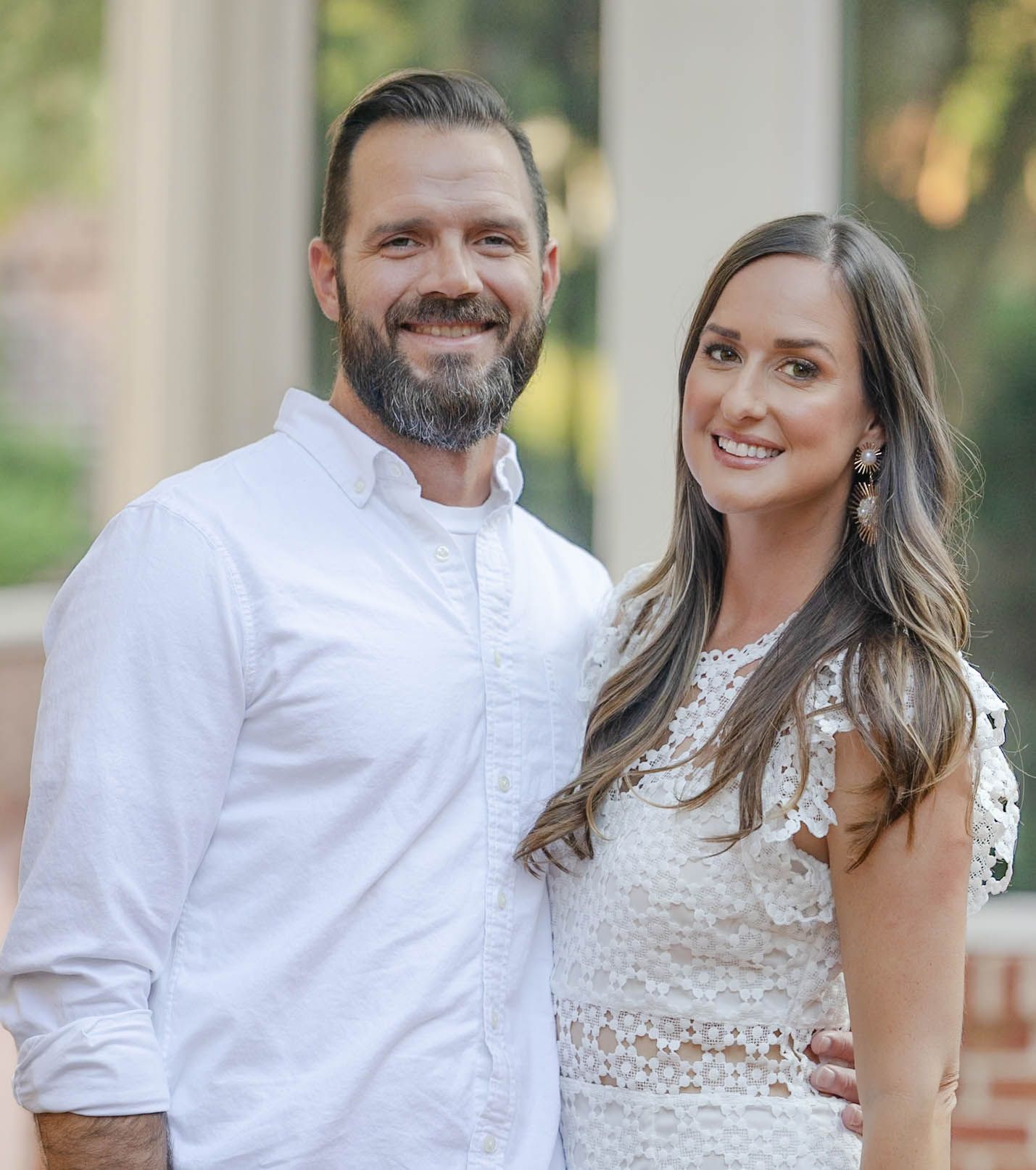 Smiling couple posing together outdoors, man in white shirt and woman in white lace dress, portrait photo.