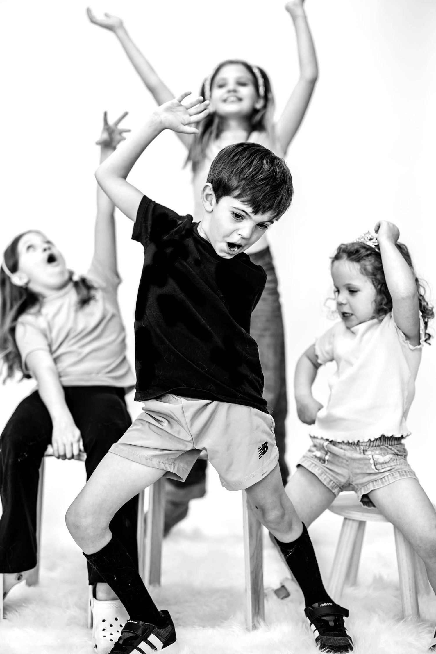 Black and white photo of four energetic children dancing and posing expressively in a studio setting.
