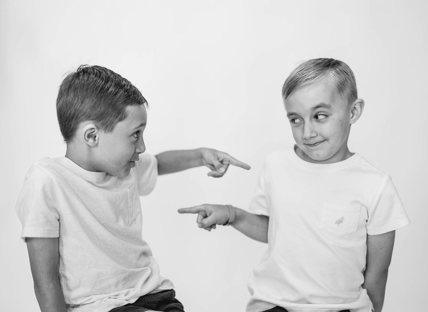 Two boys in white t-shirts pointing at each other in a black and white photo.
