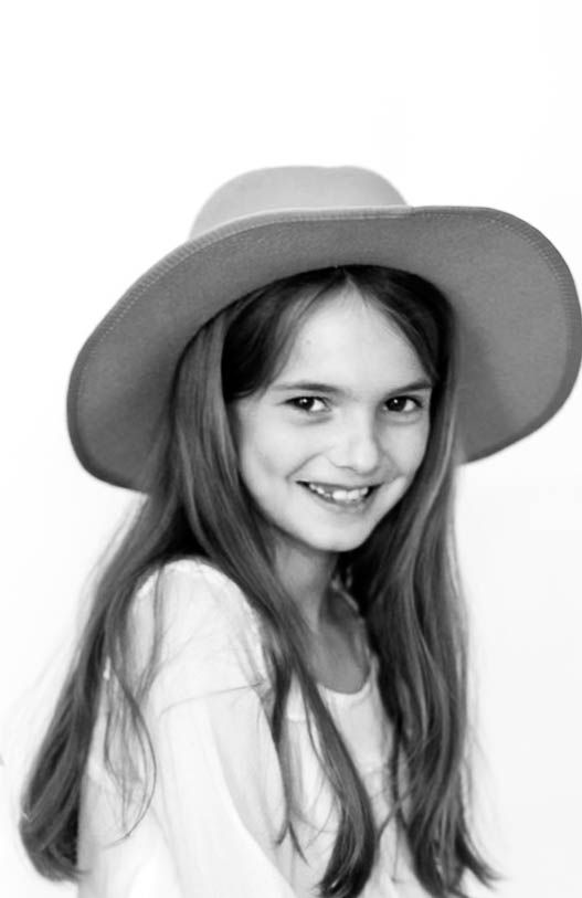 Black and white portrait of a smiling young girl with long hair wearing a wide-brim hat.