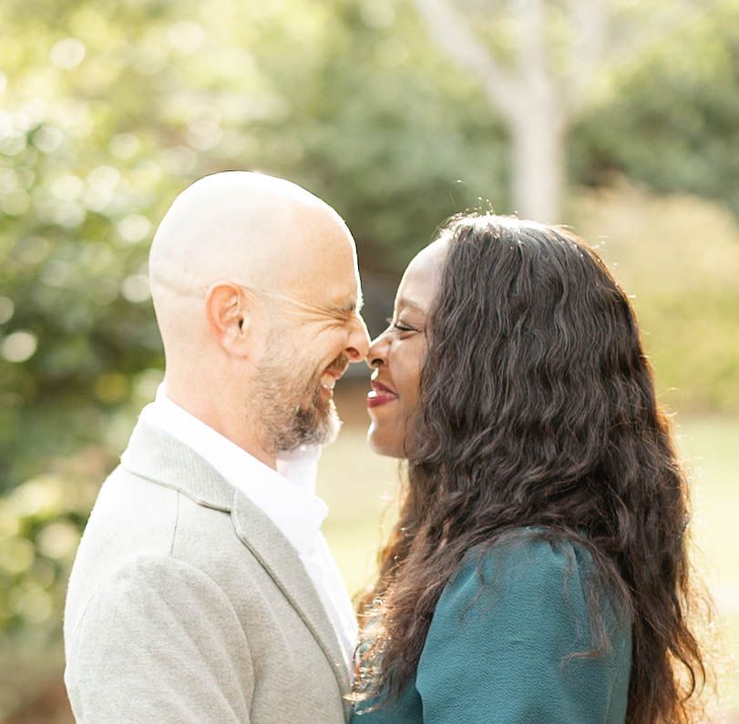 Romantic couple sharing an intimate moment nose-to-nose outdoors in a lush green garden setting.