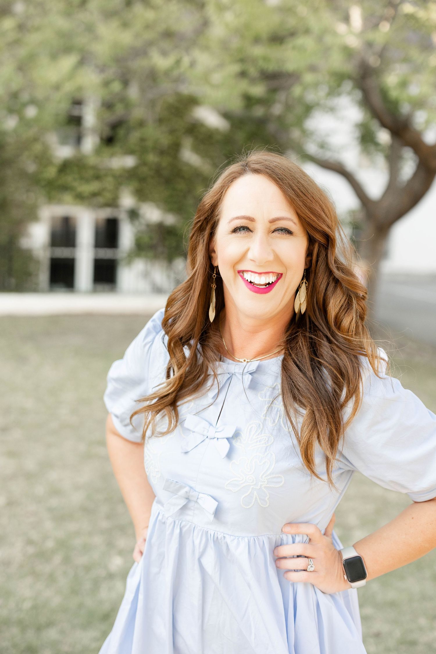 Smiling brunette woman in light blue puff sleeve dress with bow detail poses outdoors.