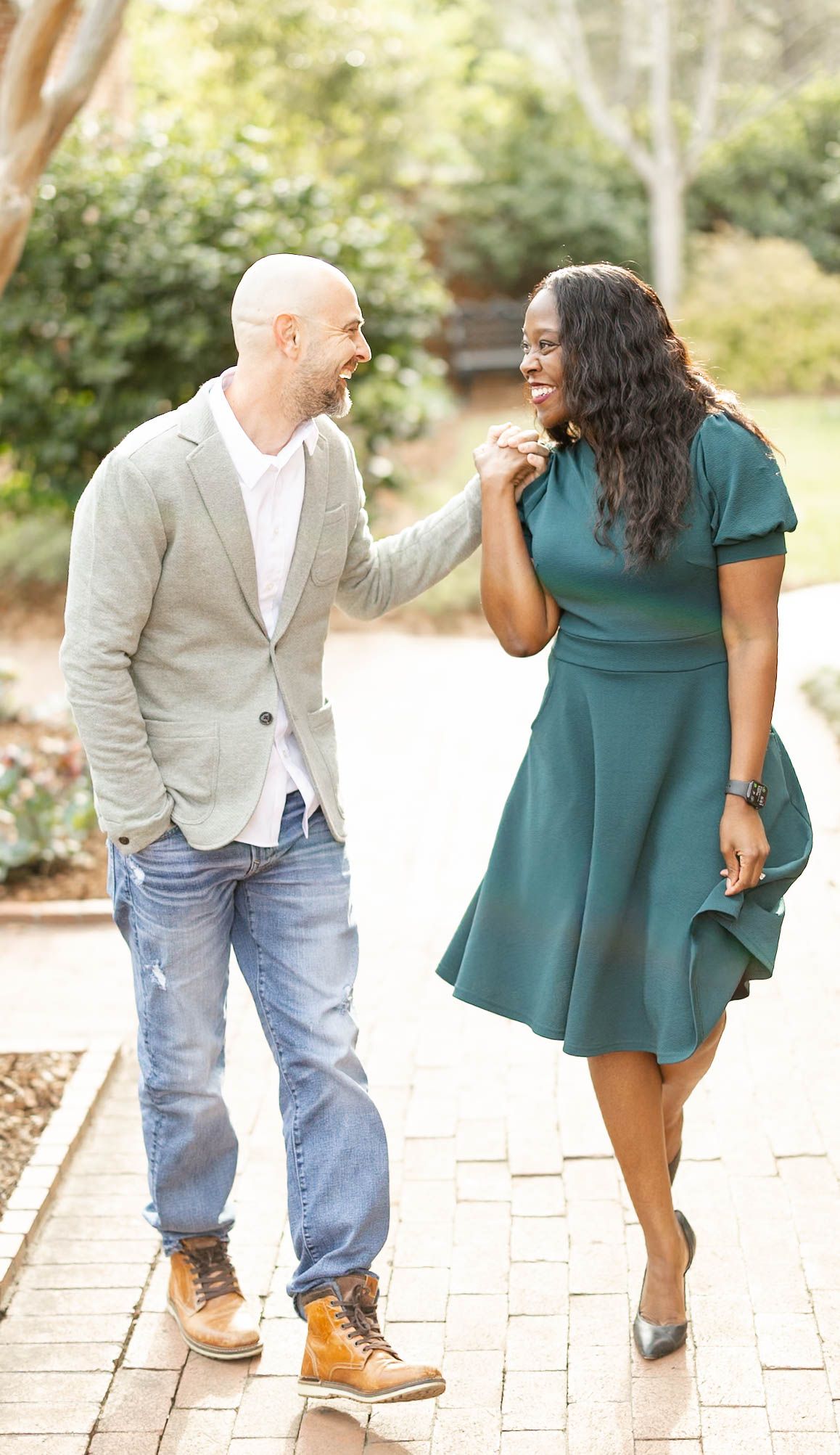 Happy interracial couple walking and laughing together on a sunlit brick pathway in a garden.